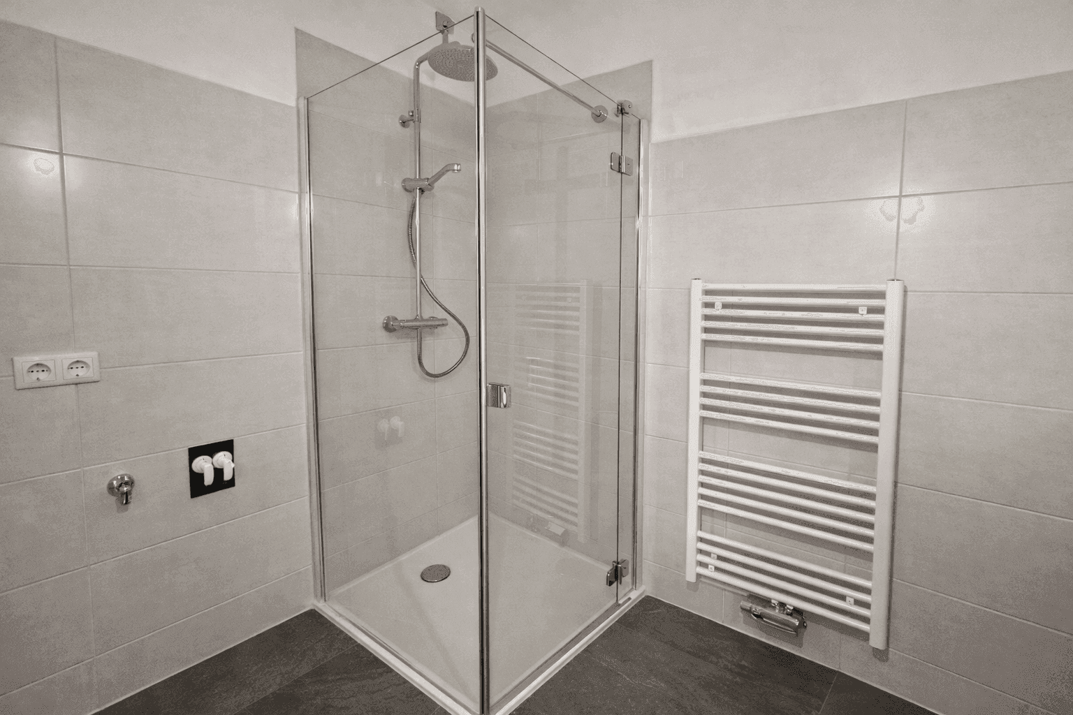 Eckdusche mit Glaswänden und Regenduschkopf in einem hell gefliesten Badezimmer mit Handtuchheizkörper.