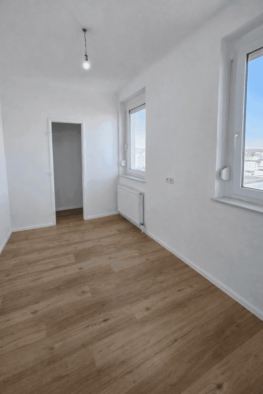 Helles Schlafzimmer mit neuem Laminatboden und zwei großen Fenstern, die viel Tageslicht hereinlassen.