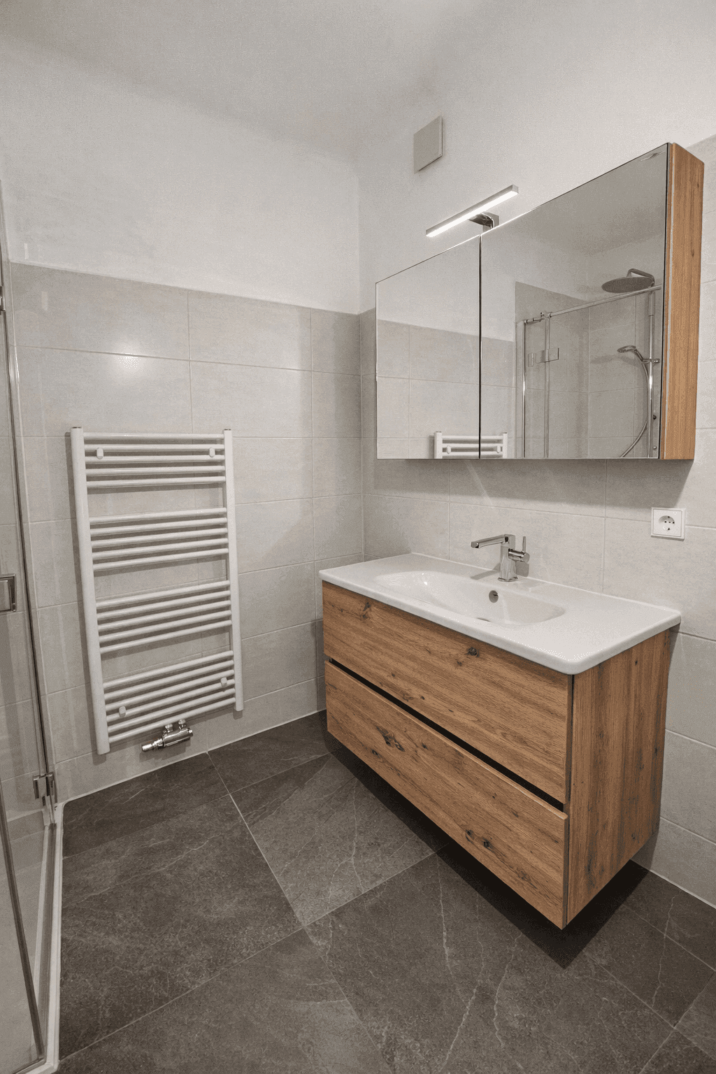 Modernes Badezimmer mit schwebendem Holzwaschtisch, Spiegelschrank und hellen Wand- und Bodenfliesen.