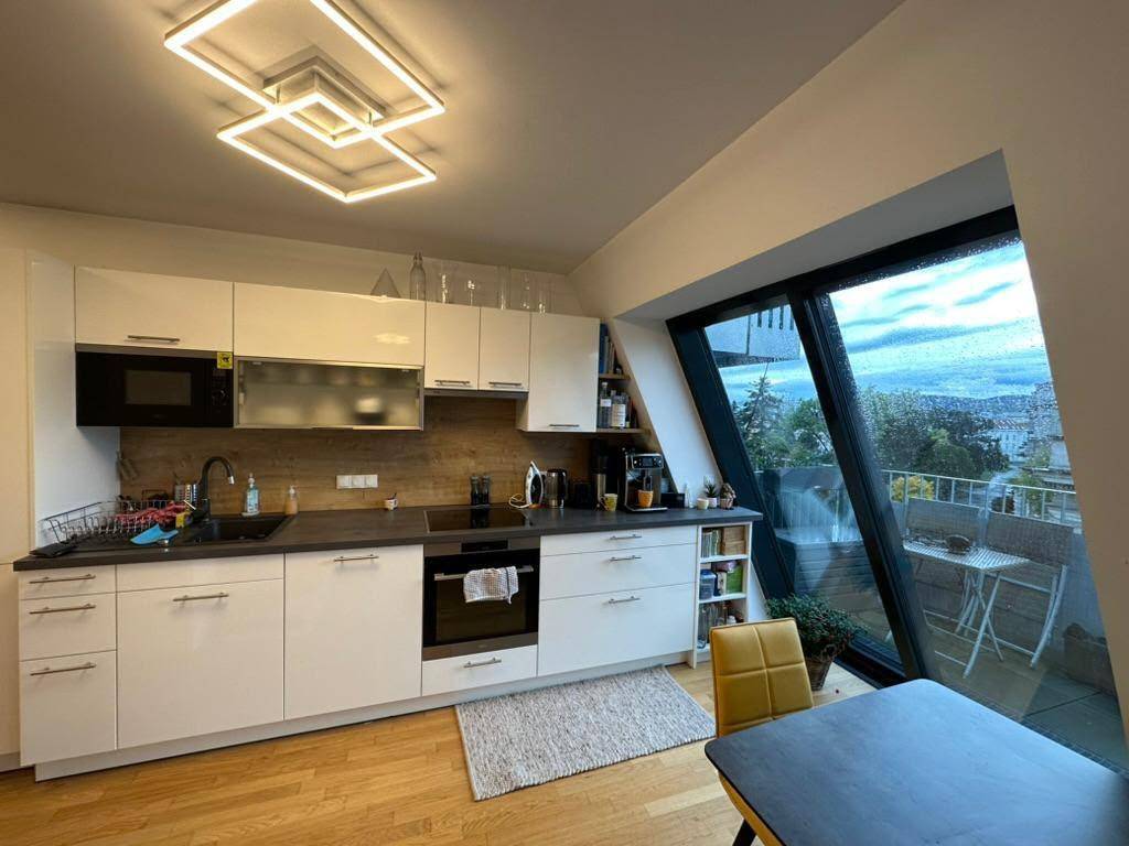 Moderne Küche mit weißen Schränken, Holzakzenten und Zugang zu einer Dachterrasse mit Ausblick.