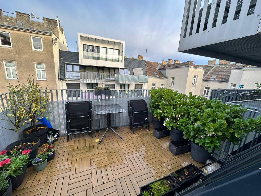 Geräumige Dachterrasse mit Holzboden, vielen Pflanzen und Blick auf die Nachbargebäude.