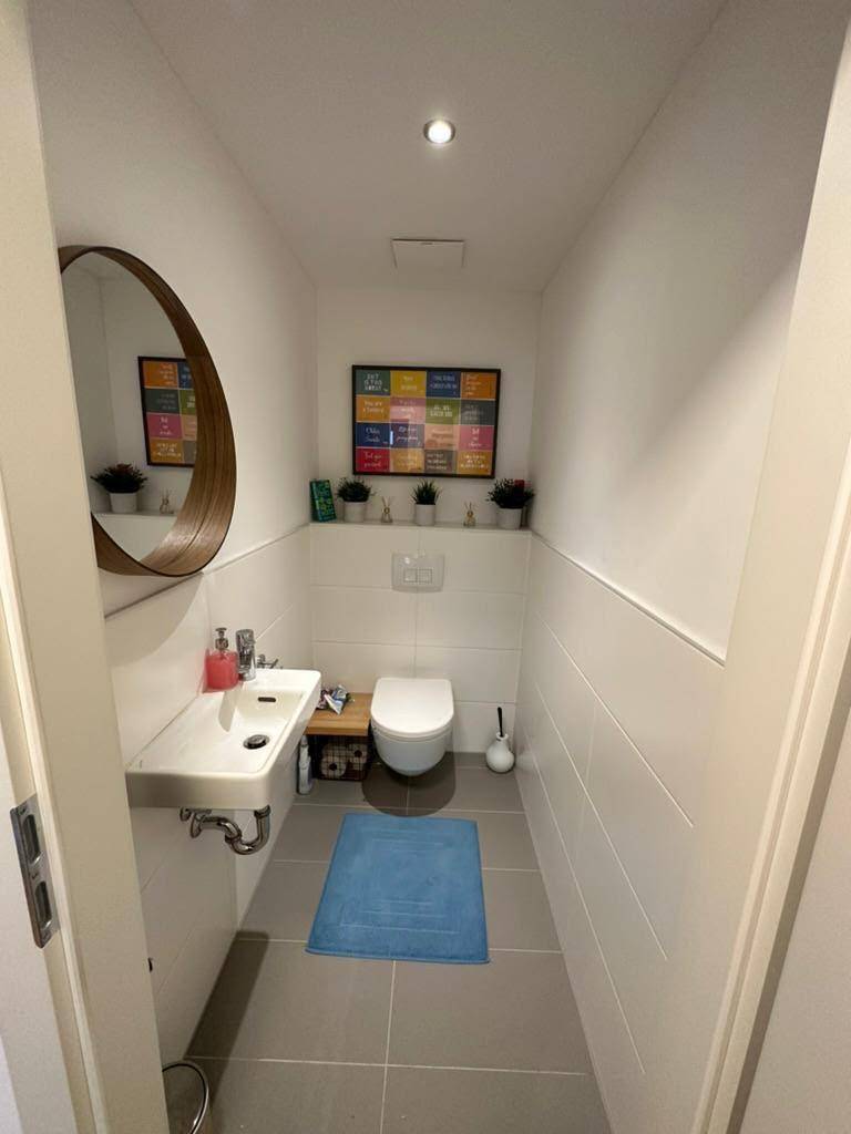Modernes Gäste-WC mit Wand-WC, kleinem Waschbecken und einem runden Holzspiegel.