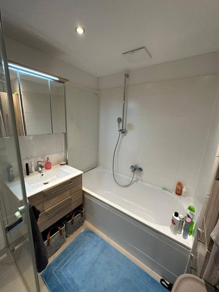 Modernes Badezimmer mit Badewanne, Dusche, Waschtisch und Spiegelschrank in hellen Farbtönen.