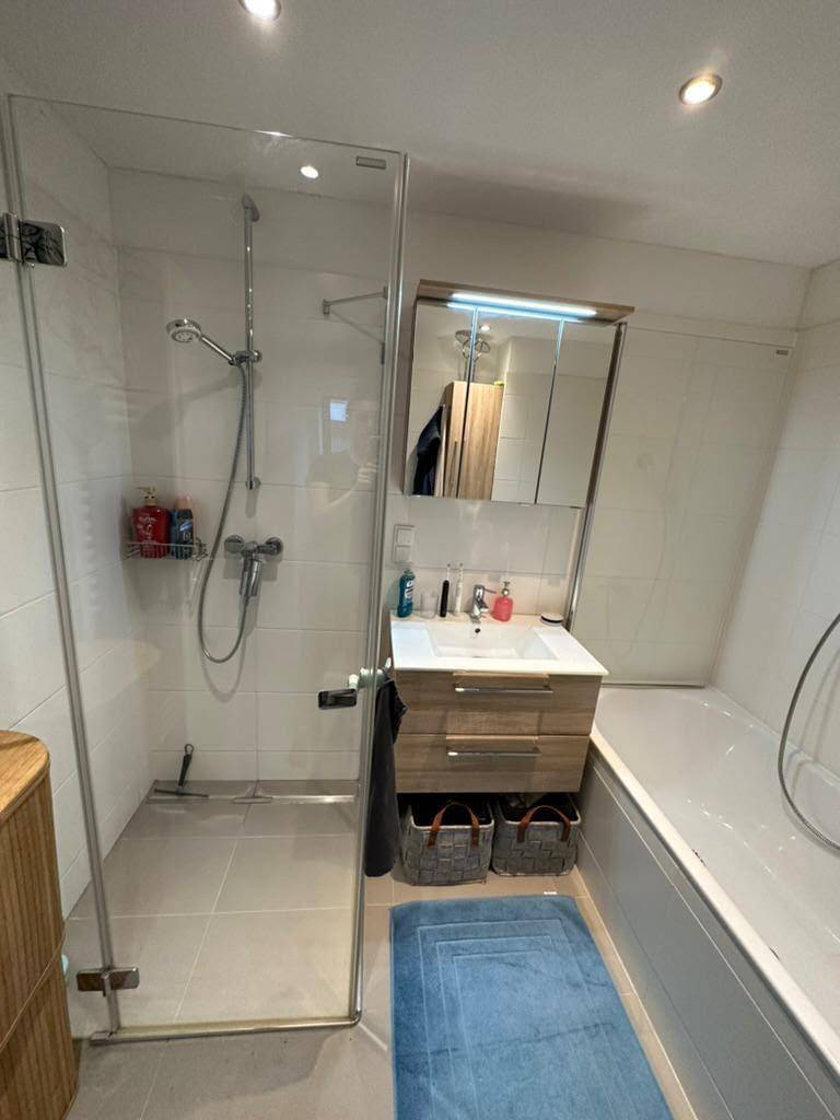 Helles Badezimmer mit Glasdusche, Badewanne und Spiegelschrank über dem Waschbecken für Stauraum.