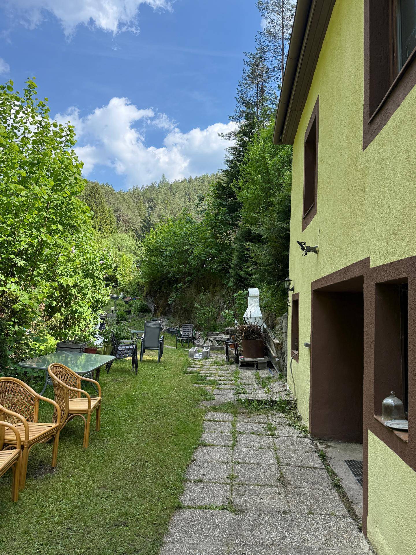 Seitenansicht des Hauses mit Rasenfläche und verschiedenen Gartenmöbeln unter blauem Himmel.