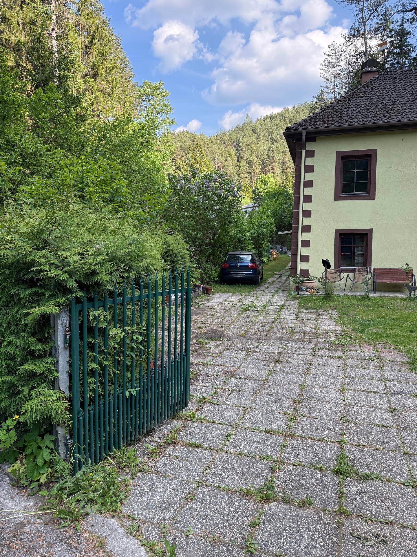Zufahrt zum Haus mit gepflastertem Weg, umgeben von üppigem Grün und Bäumen.