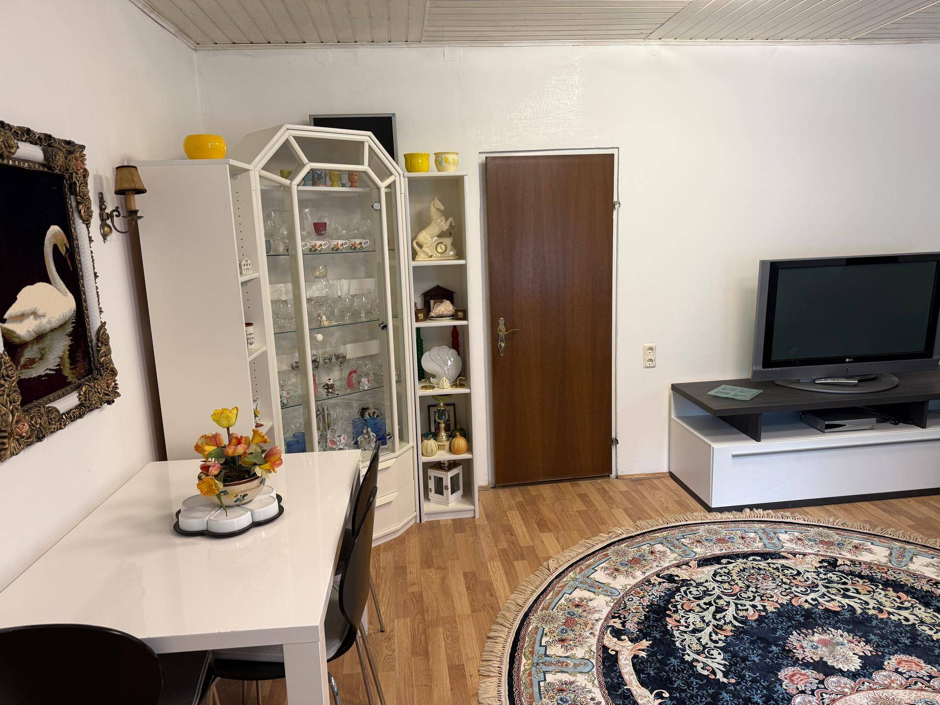 Heller Wohn- und Essbereich mit modernem Esstisch, Vitrine und einem runden Teppich.