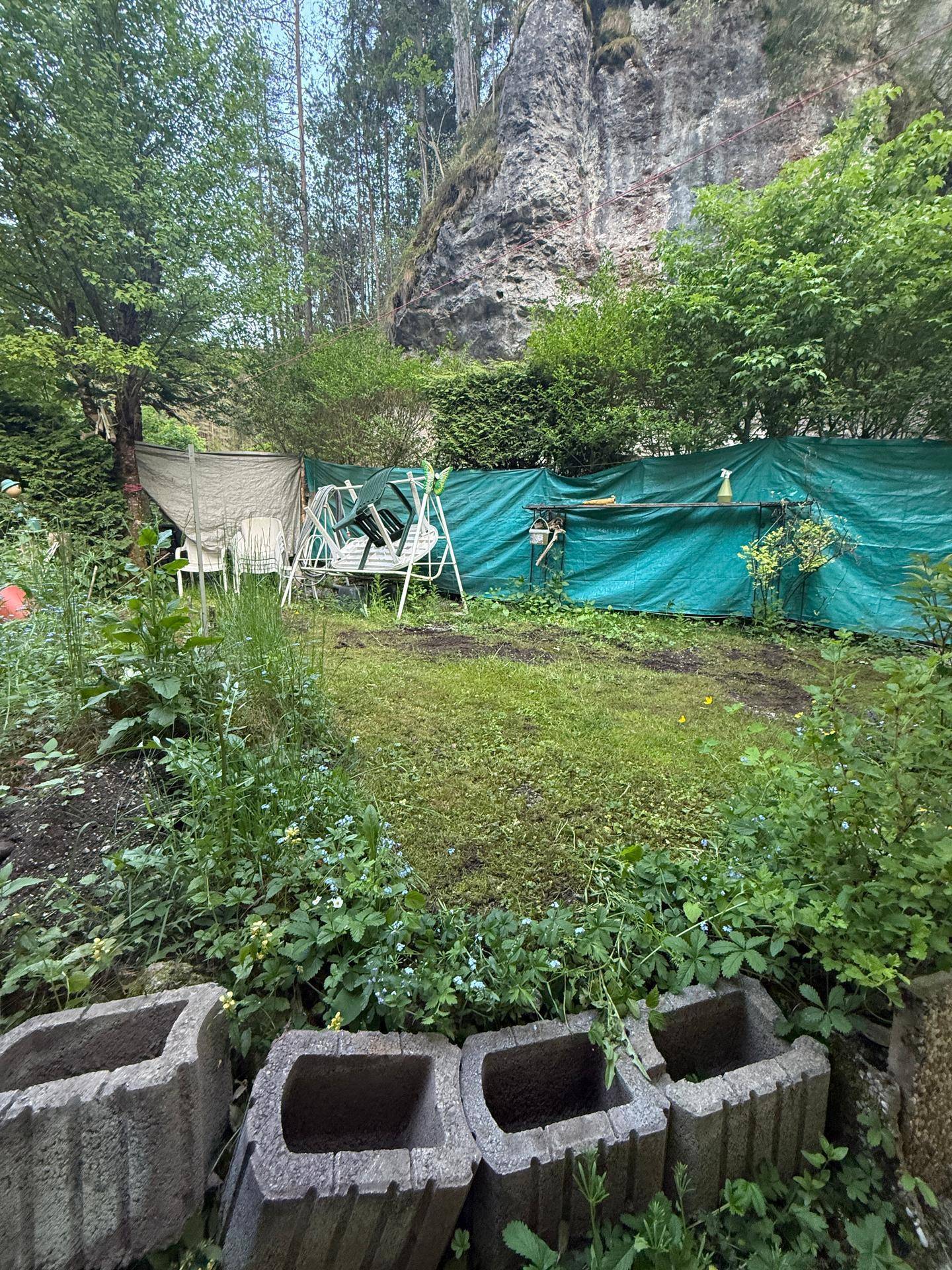 Rasenfläche im Garten mit einer Schaukel und einer natürlichen Felswand im Hintergrund.