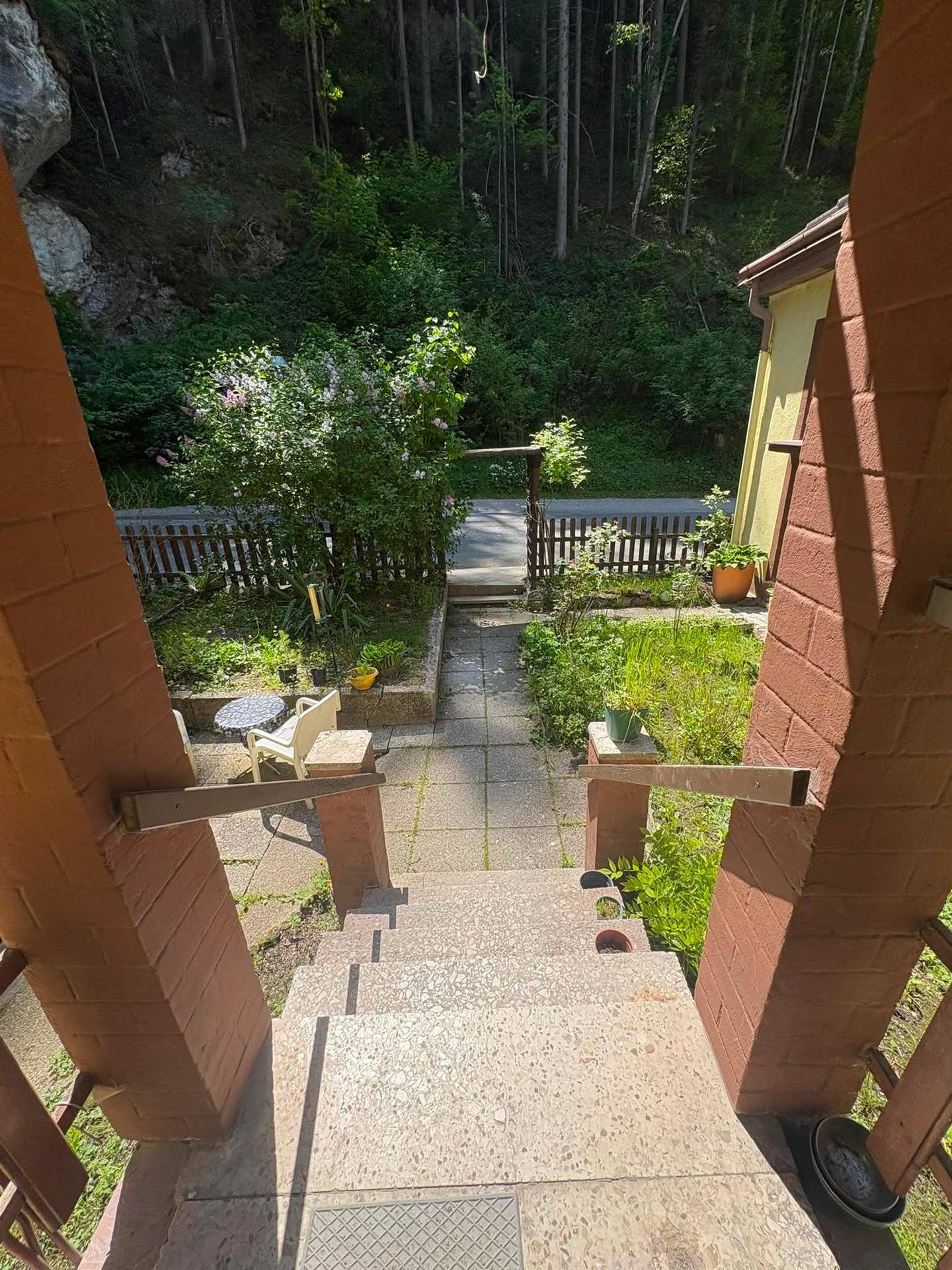 Blick von den Eingangsstufen über den Gartenbereich mit Holzzaun und der dahinterliegenden Straße.