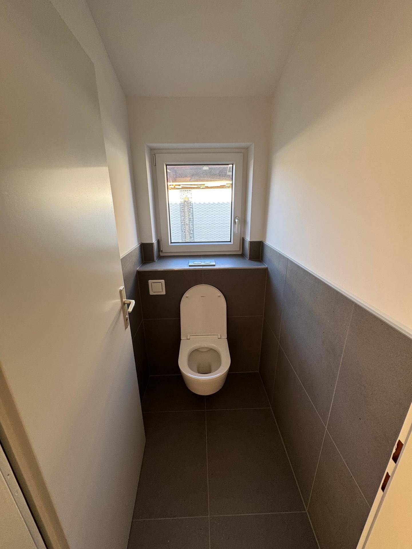 Separates Gäste-WC mit Fenster und moderner Wandtoilette in schlichtem Design.