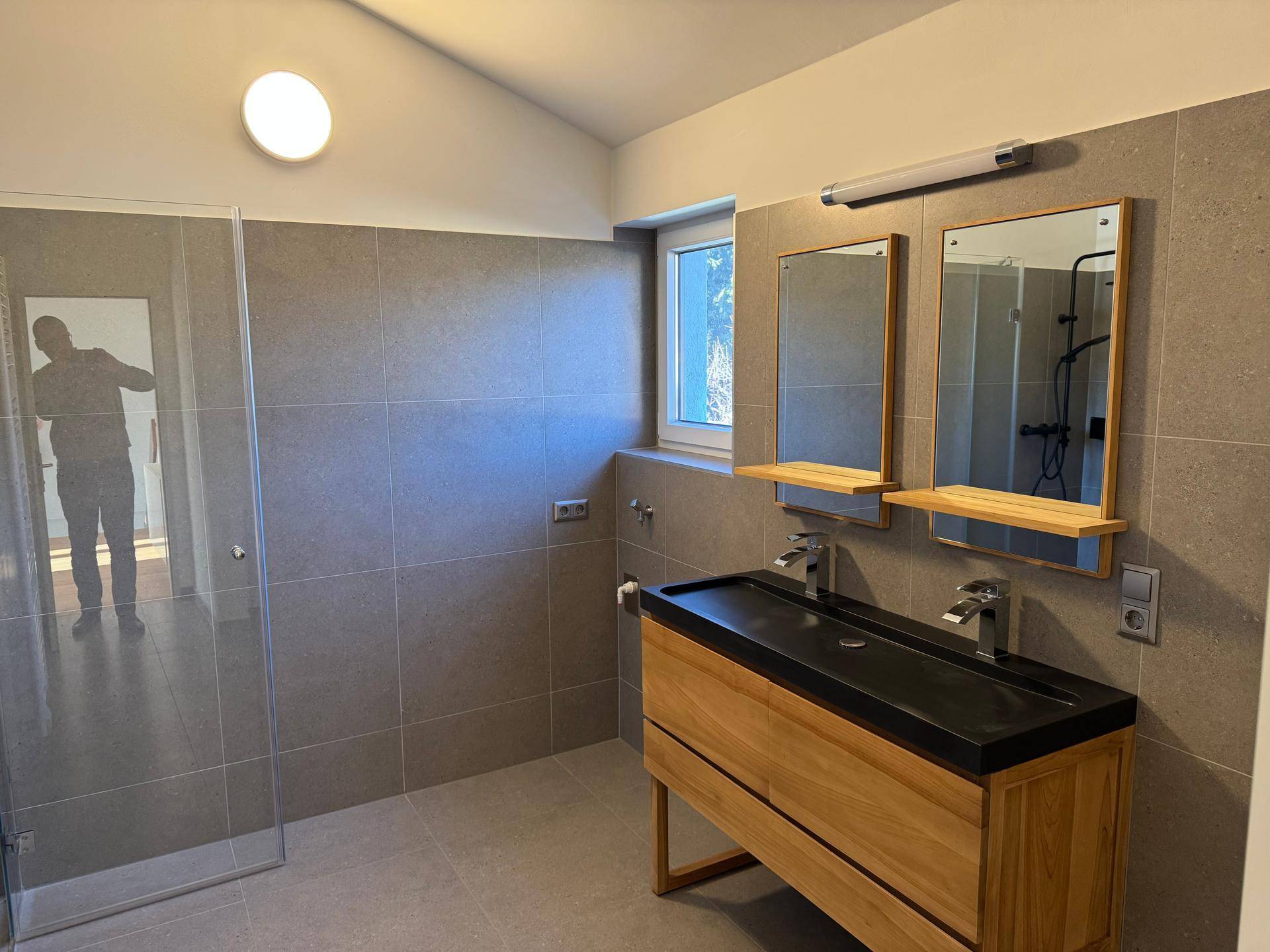 Modernes Badezimmer mit Doppelwaschbecken, begehbarer Dusche und Fenster für Tageslicht.