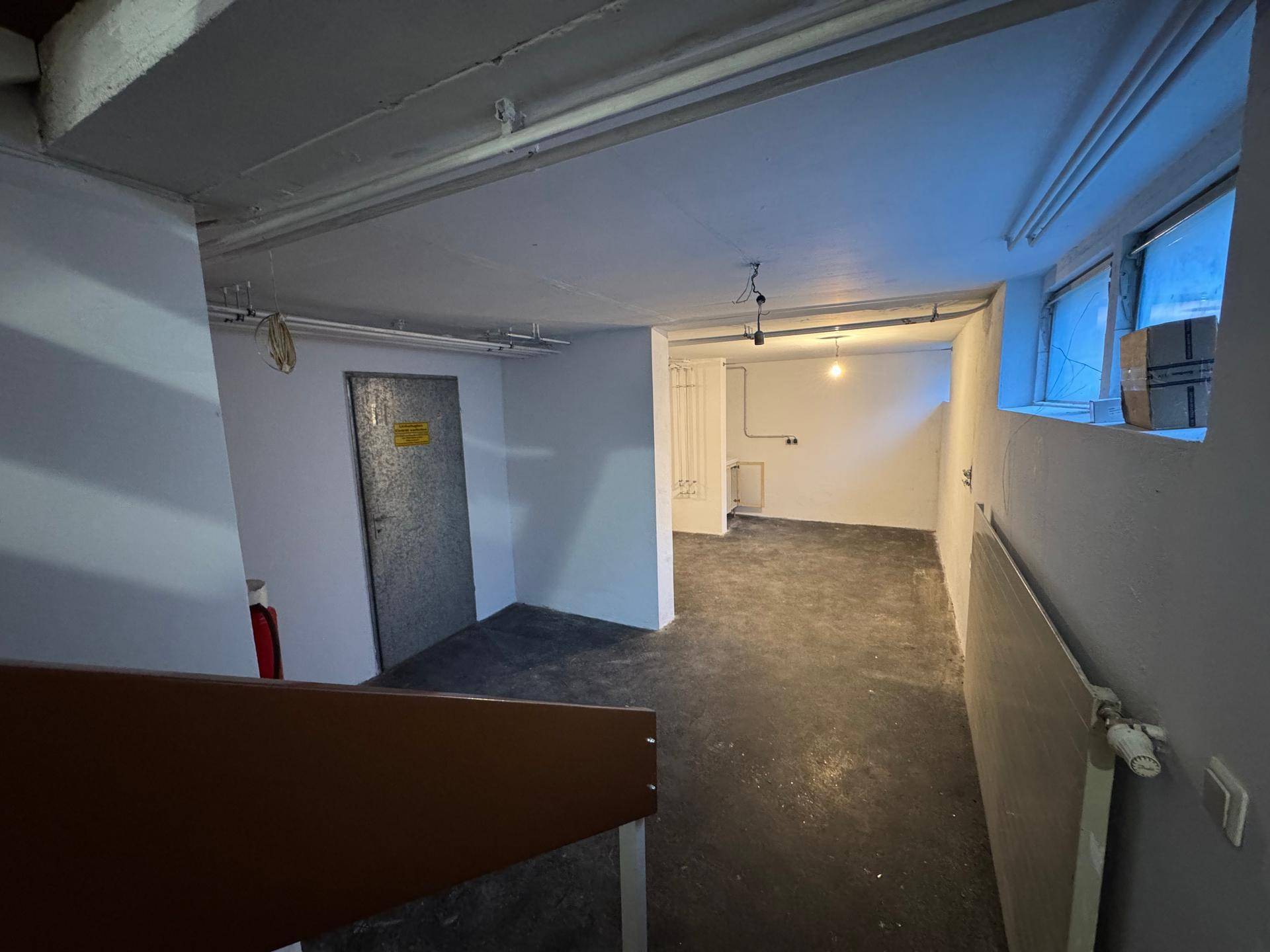 Geräumiger Kellerraum mit Betonboden und kleinen Fenstern, ideal als Abstellraum.