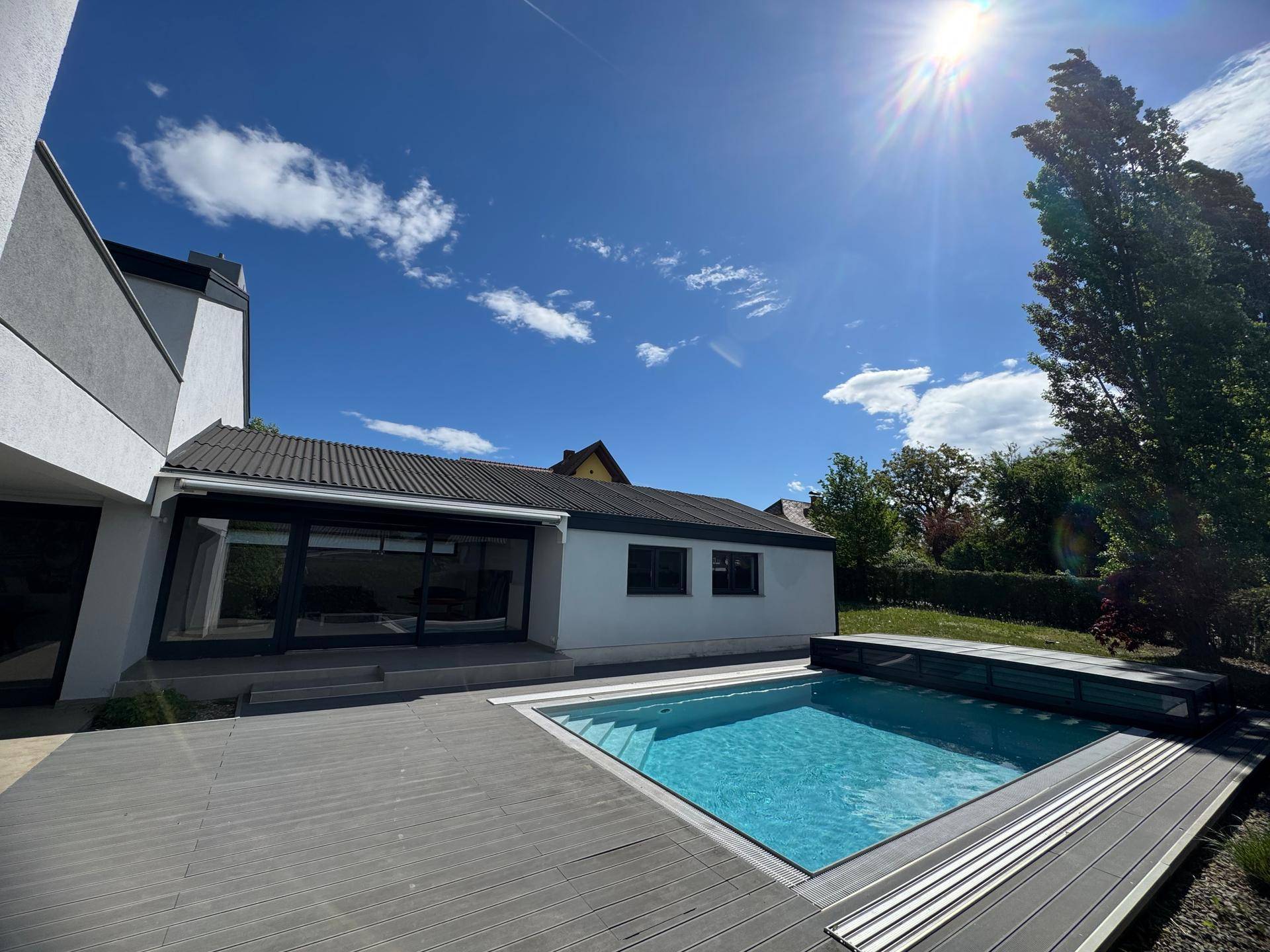 Sonniger Außenbereich mit Pool und Holzterrasse, ideal für Entspannung und Freizeitaktivitäten.