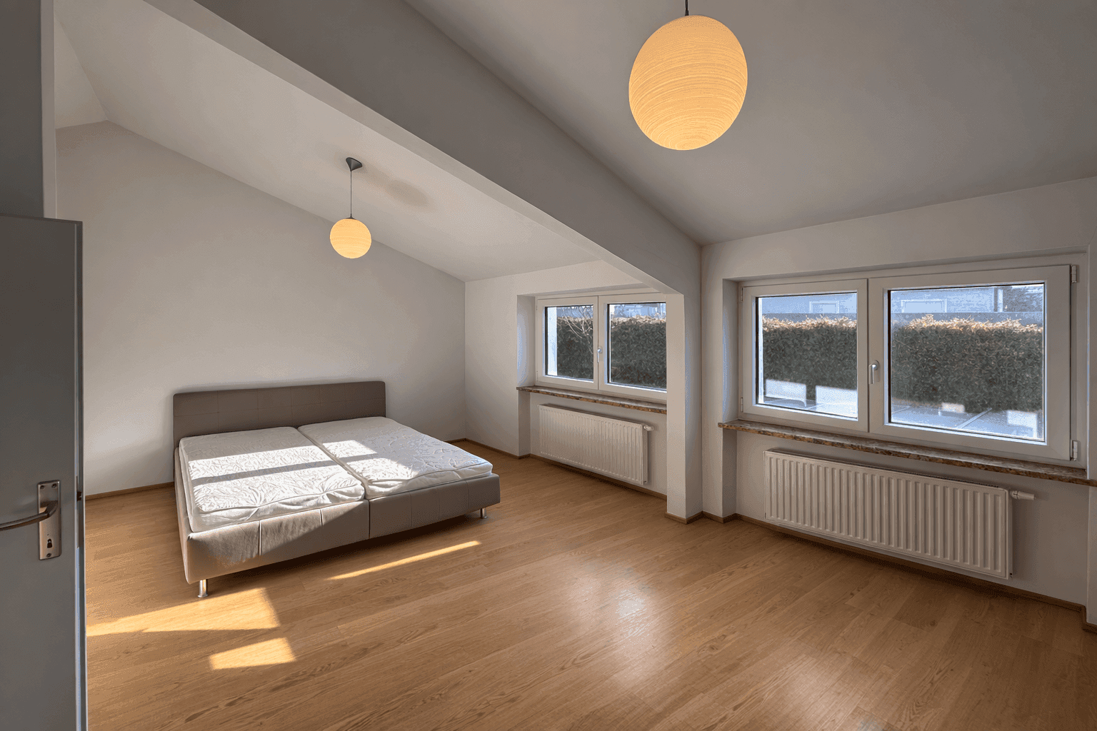 Geräumiges Schlafzimmer mit Holzboden, Dachschräge und großen Fenstern für viel Licht.