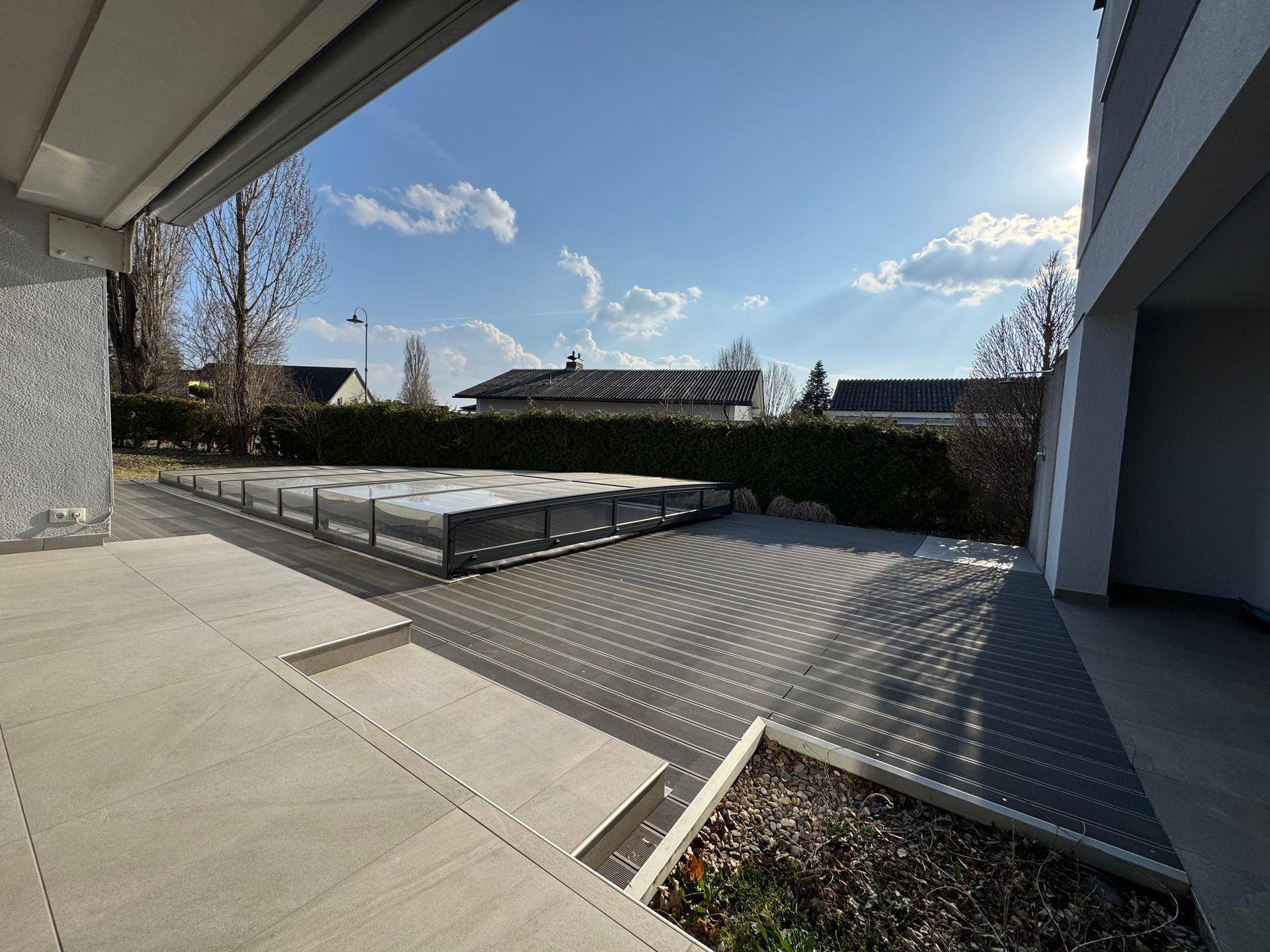 Geräumige Terrasse mit modernen Fliesen und Holzdeck, inklusive überdachtem Poolbereich.