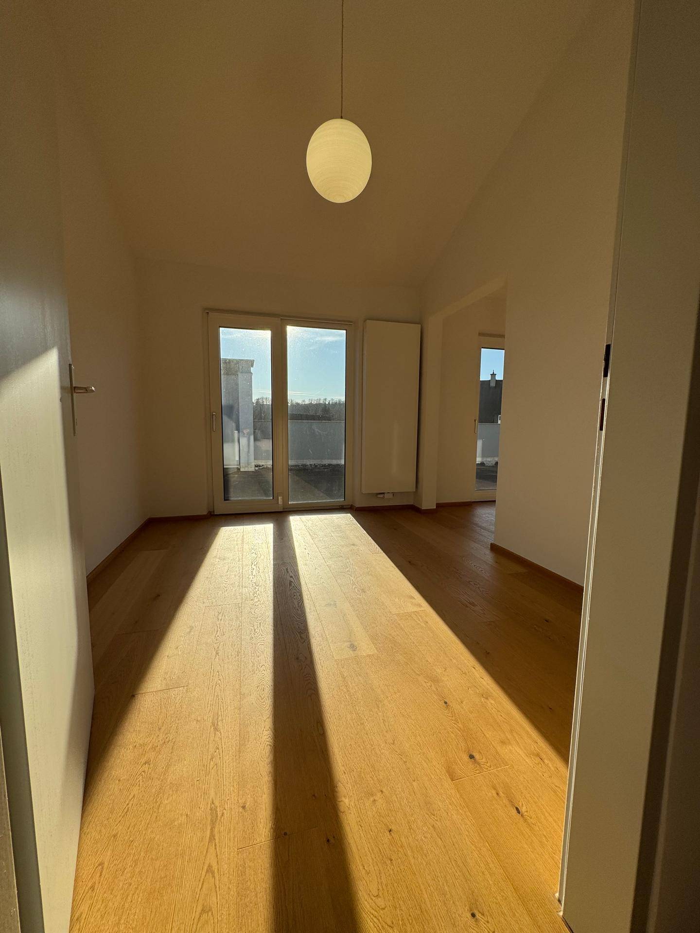 Heller Raum mit Holzboden und direktem Zugang zu einem sonnigen Balkon.