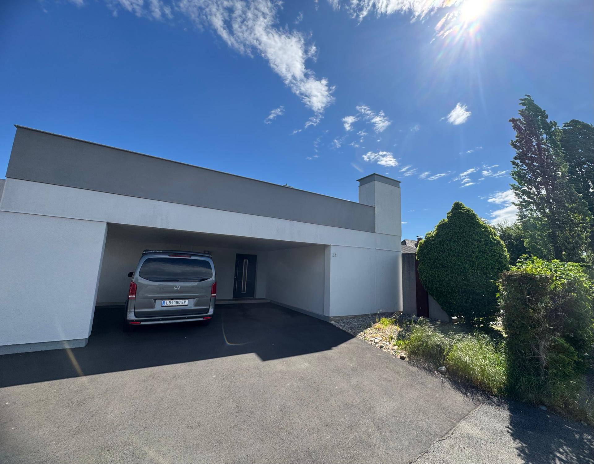 Moderne Hausfassade mit Carport und gepflegter Grünanlage unter strahlend blauem Himmel.