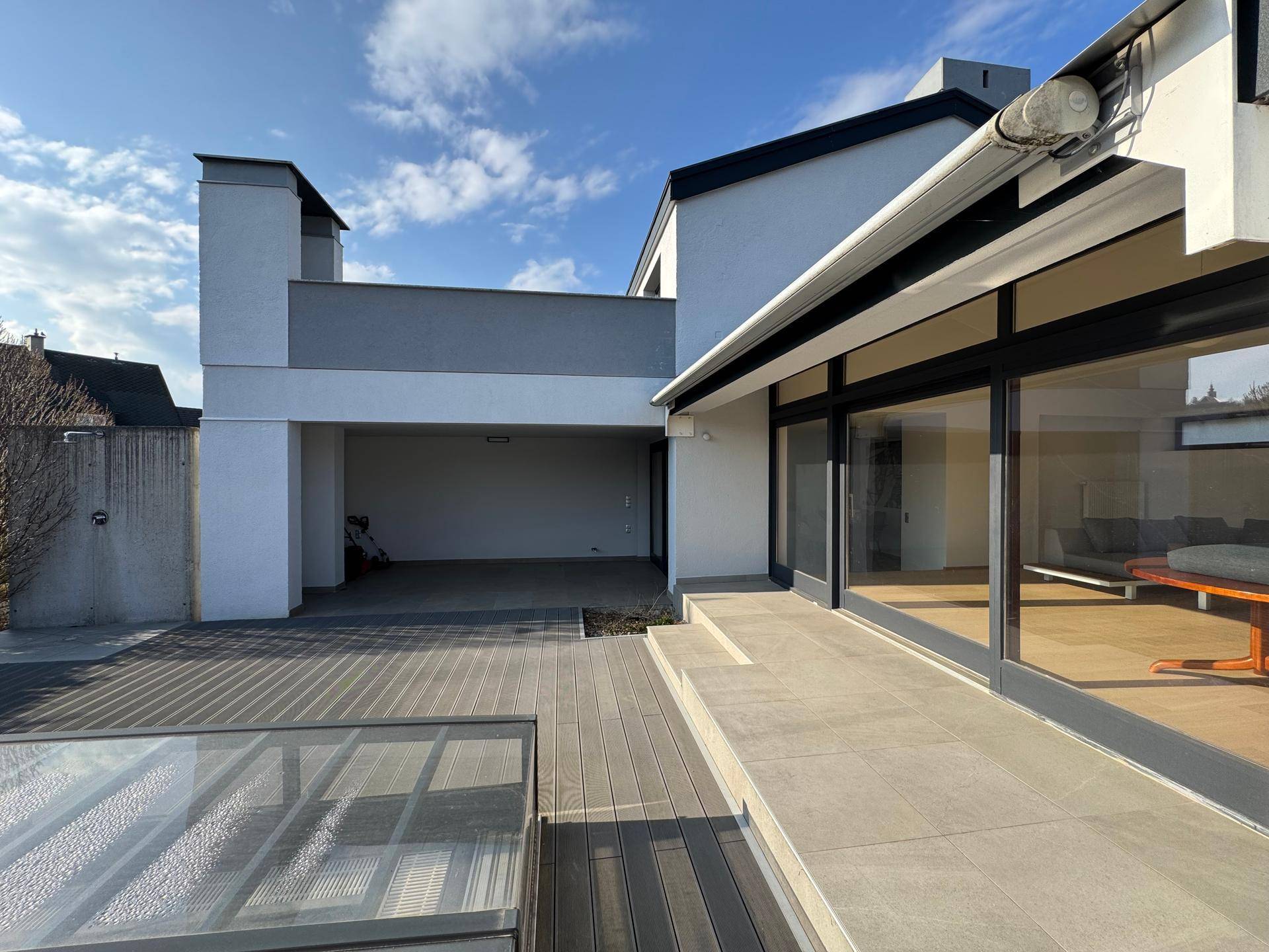 Moderne Hausfassade mit großen Glasfronten, Terrasse und überdachtem Stellplatzbereich.