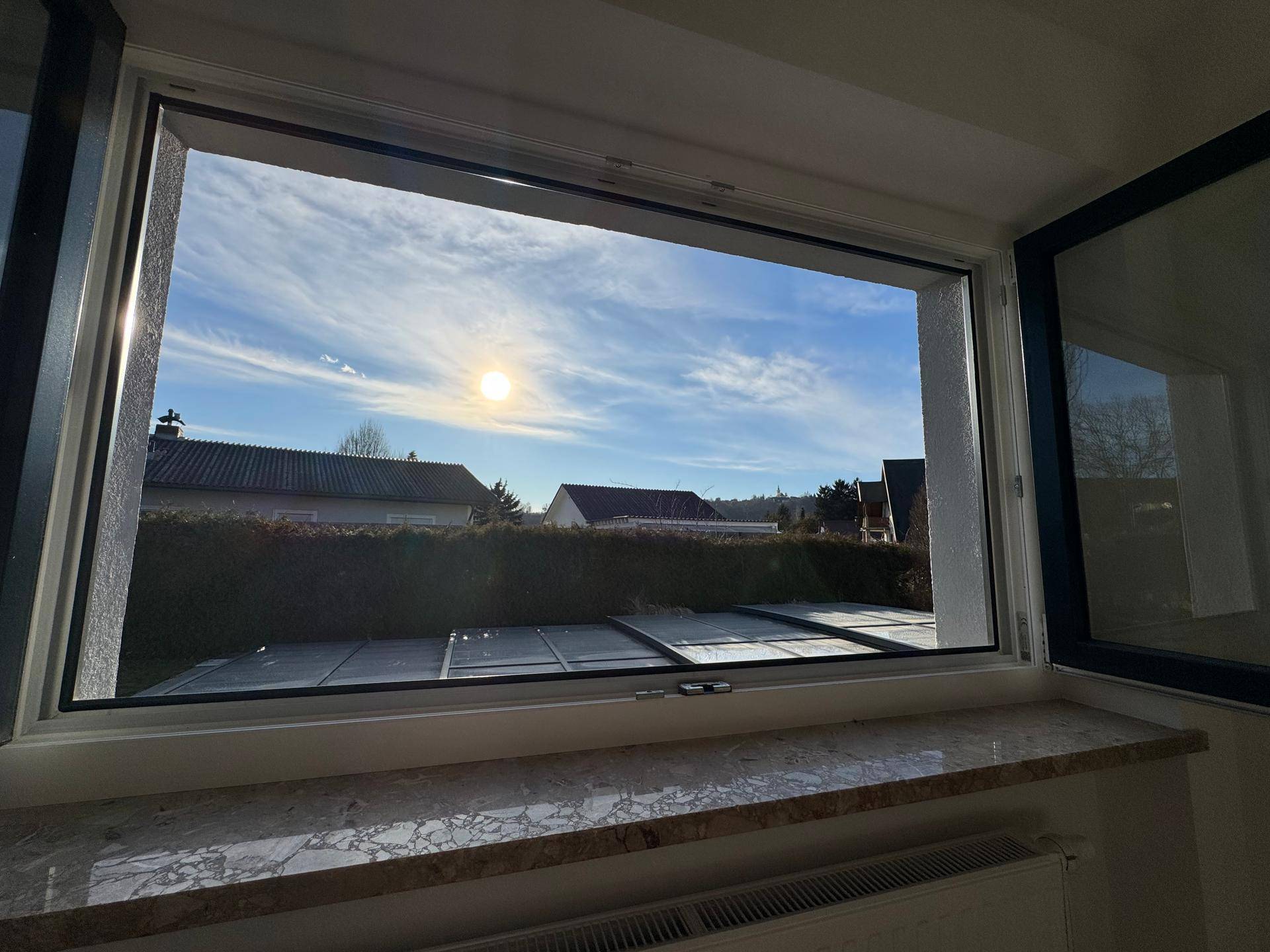 Sonniger Ausblick aus dem Fenster auf den Poolbereich und die umliegende Landschaft.