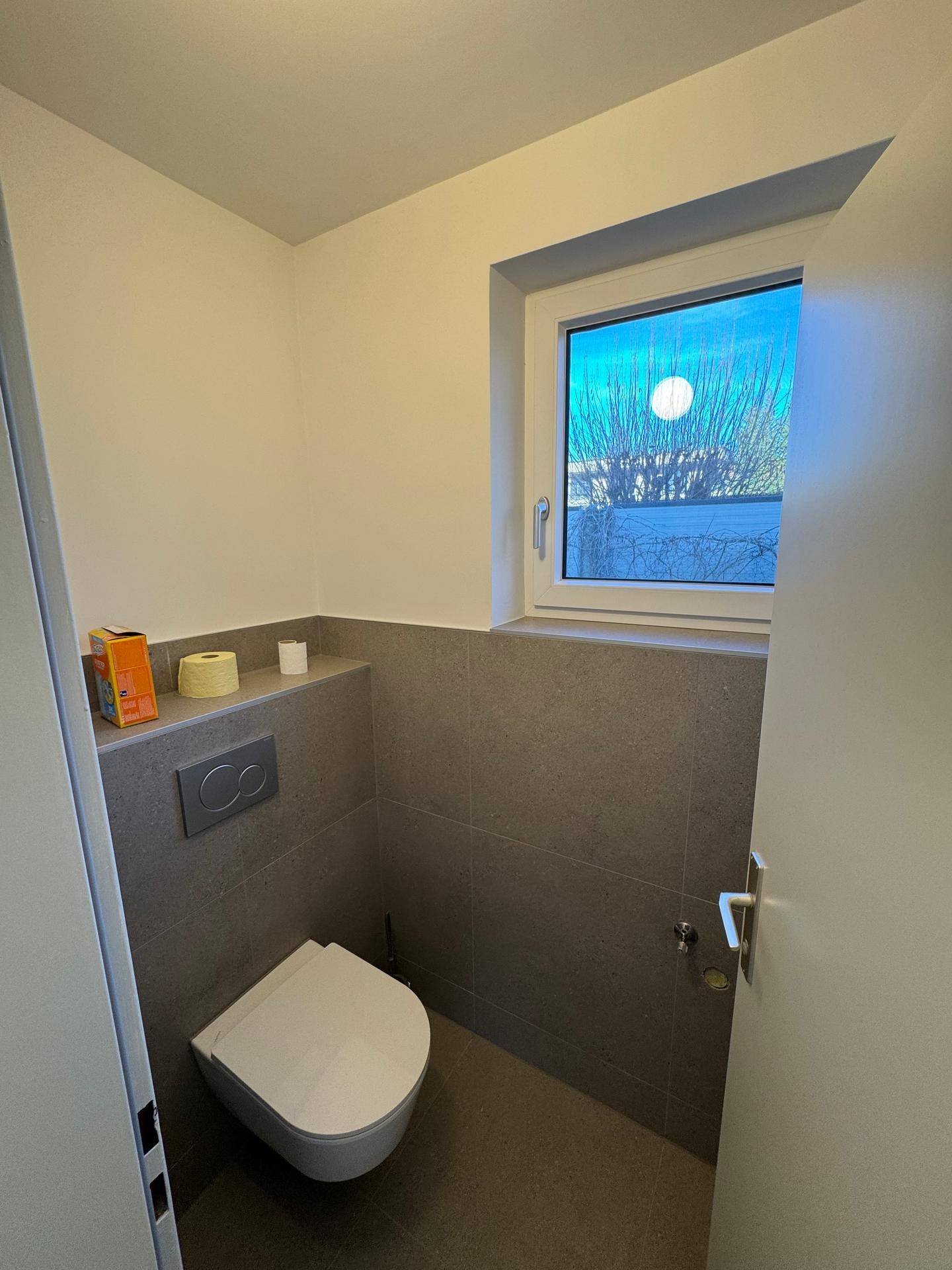 Helles Gäste-WC mit Fenster und moderner Wandtoilette in neutralen Farben.