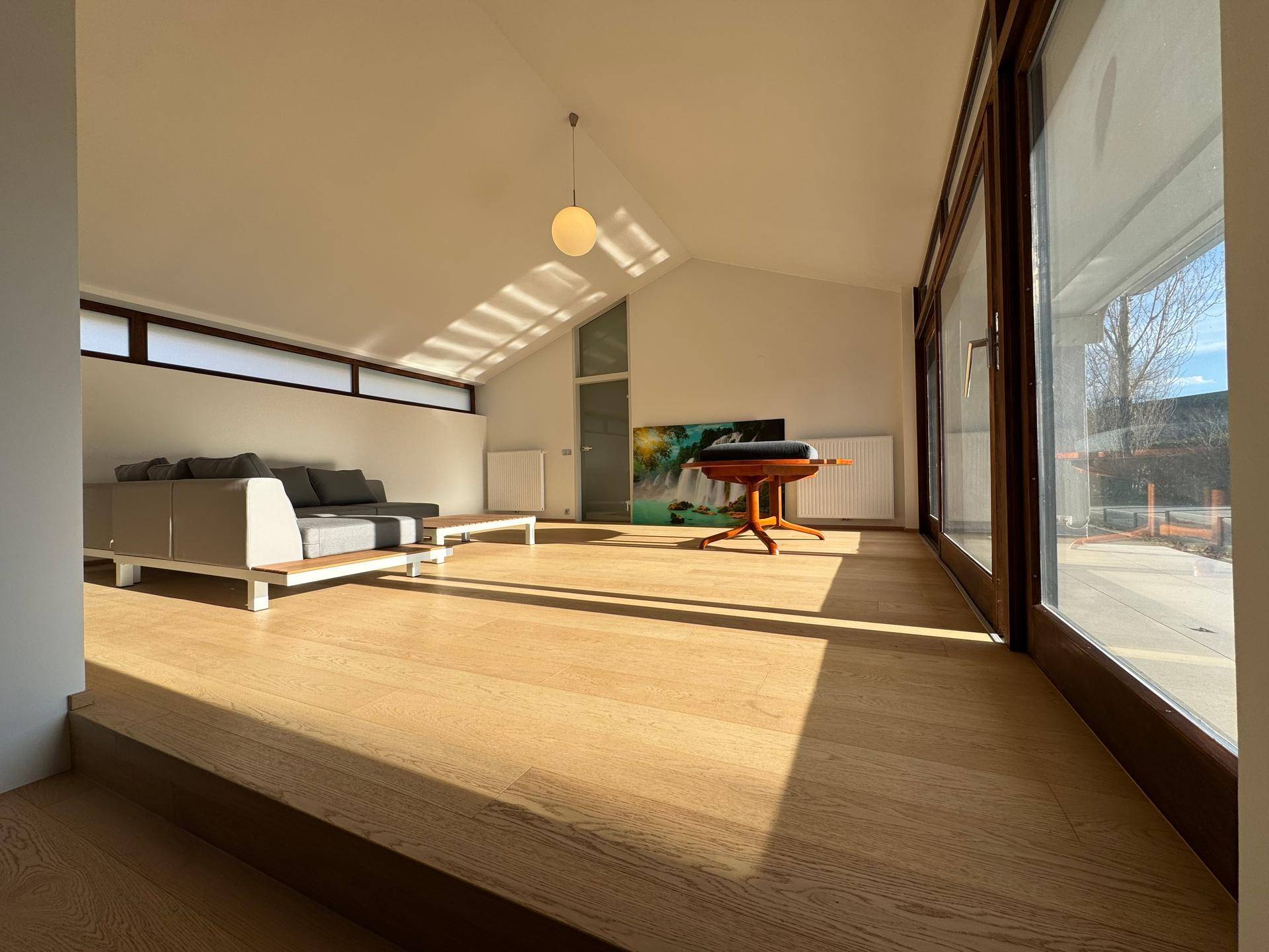 Lichtdurchflutetes Wohnzimmer mit Holzboden, hohen Decken und großen Fenstern.