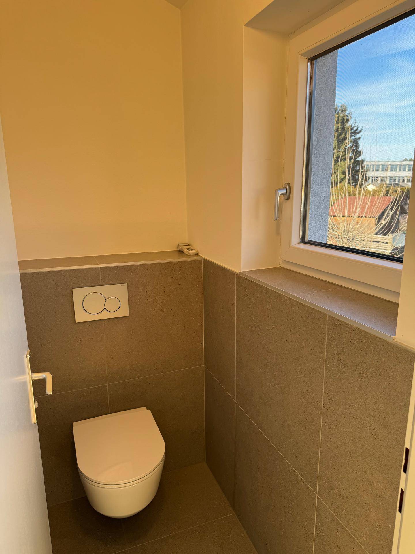 Modernes Gäste-WC mit Fenster und Wandtoilette in schlichtem, funktionalem Design.