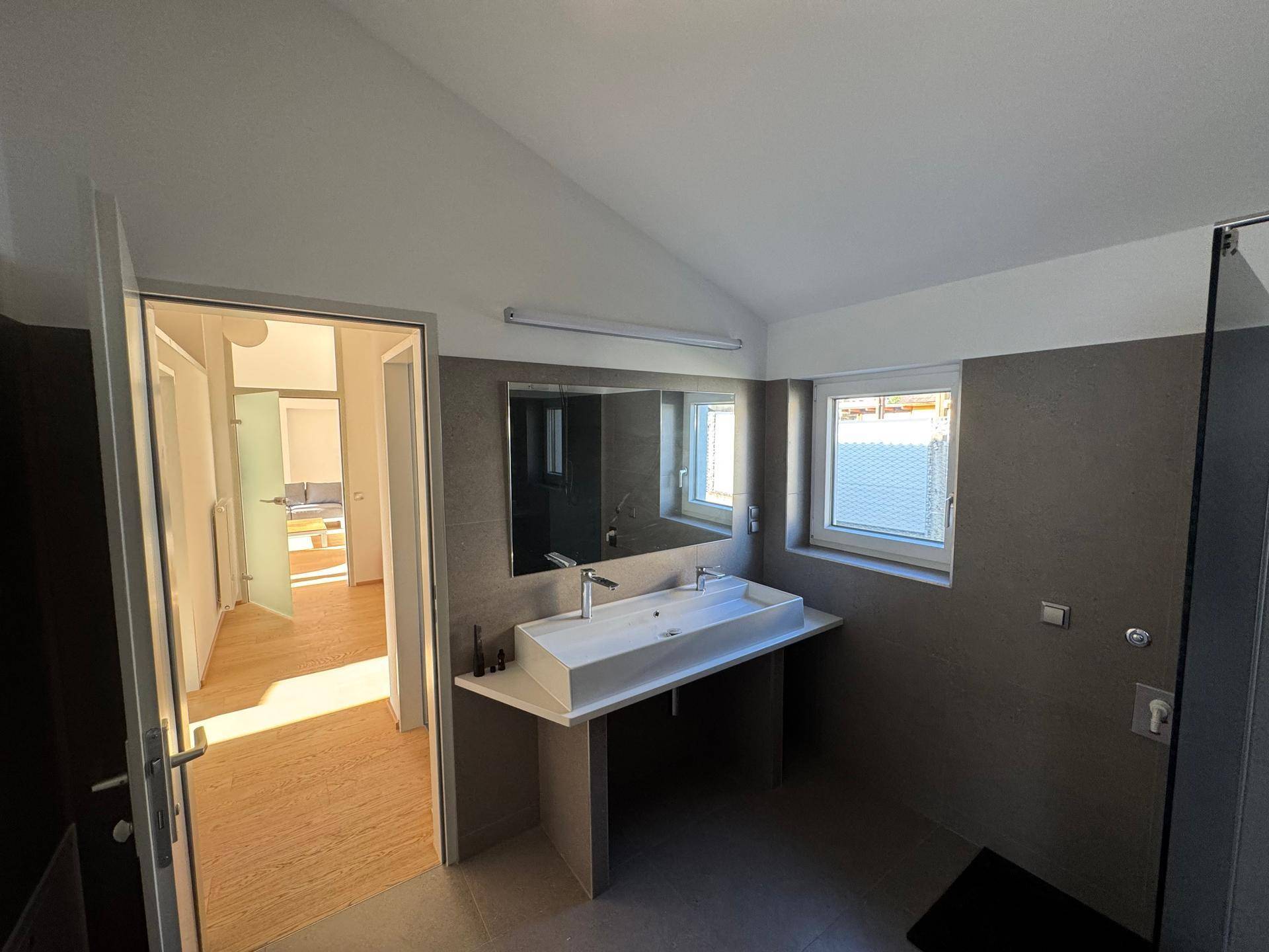 Modernes Badezimmer mit Doppelwaschbecken, Fliesen und einem Fenster für Tageslicht.