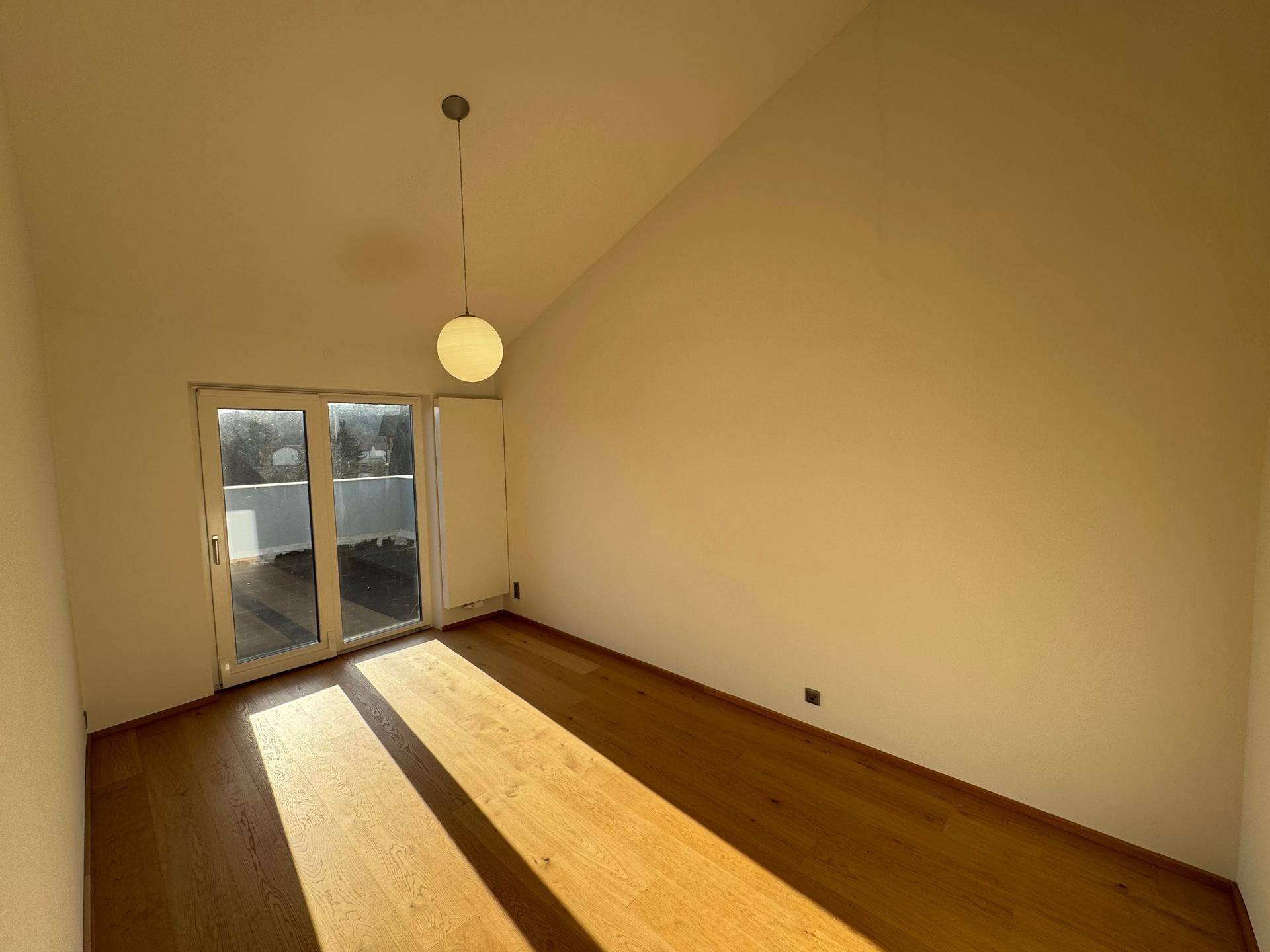 Heller Raum mit Dachschräge, Holzboden und Zugang zu einem Außenbereich.