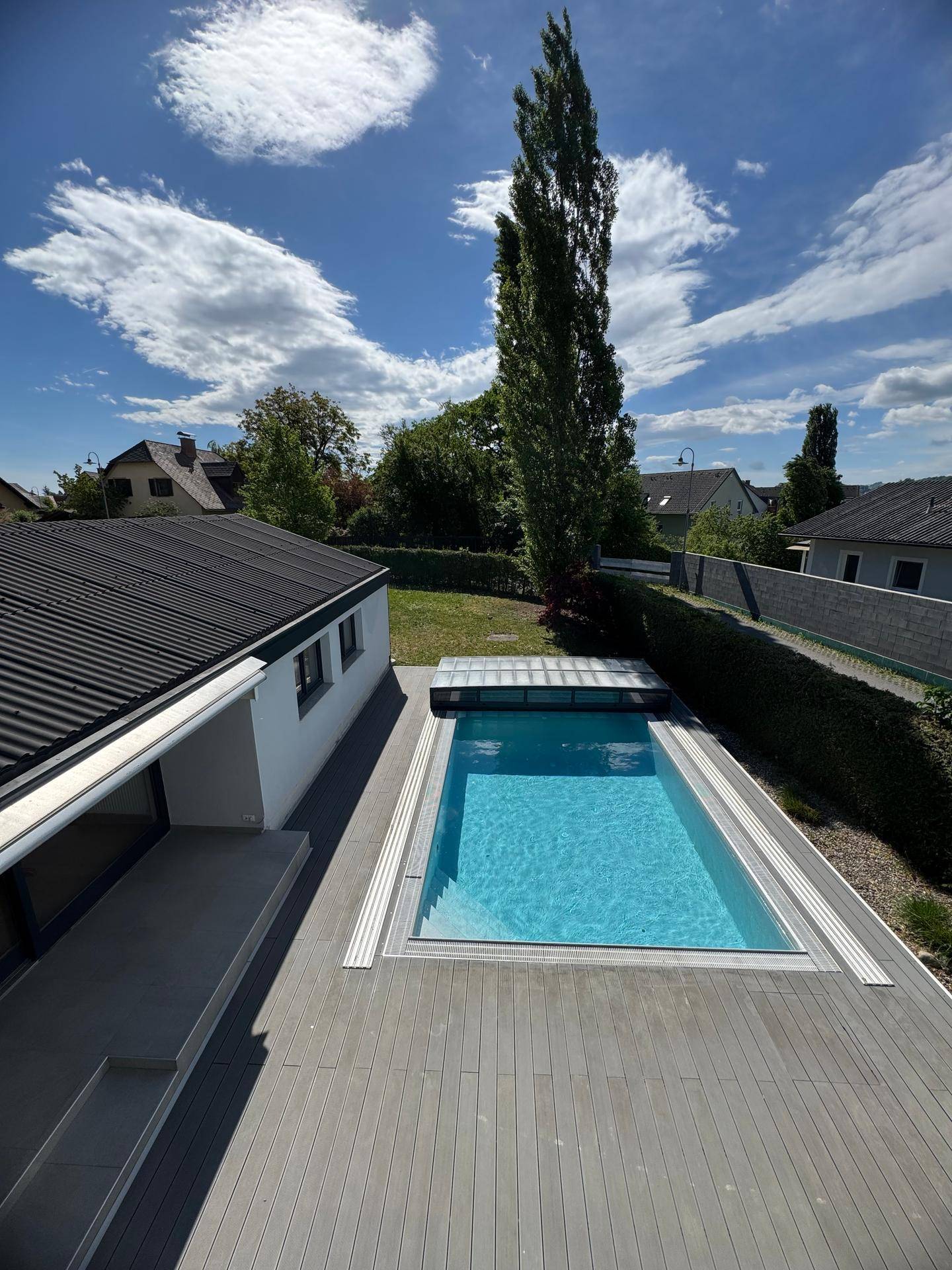 Vogelperspektive auf den Poolbereich mit Holzdeck und dem modernen Haus im Hintergrund.