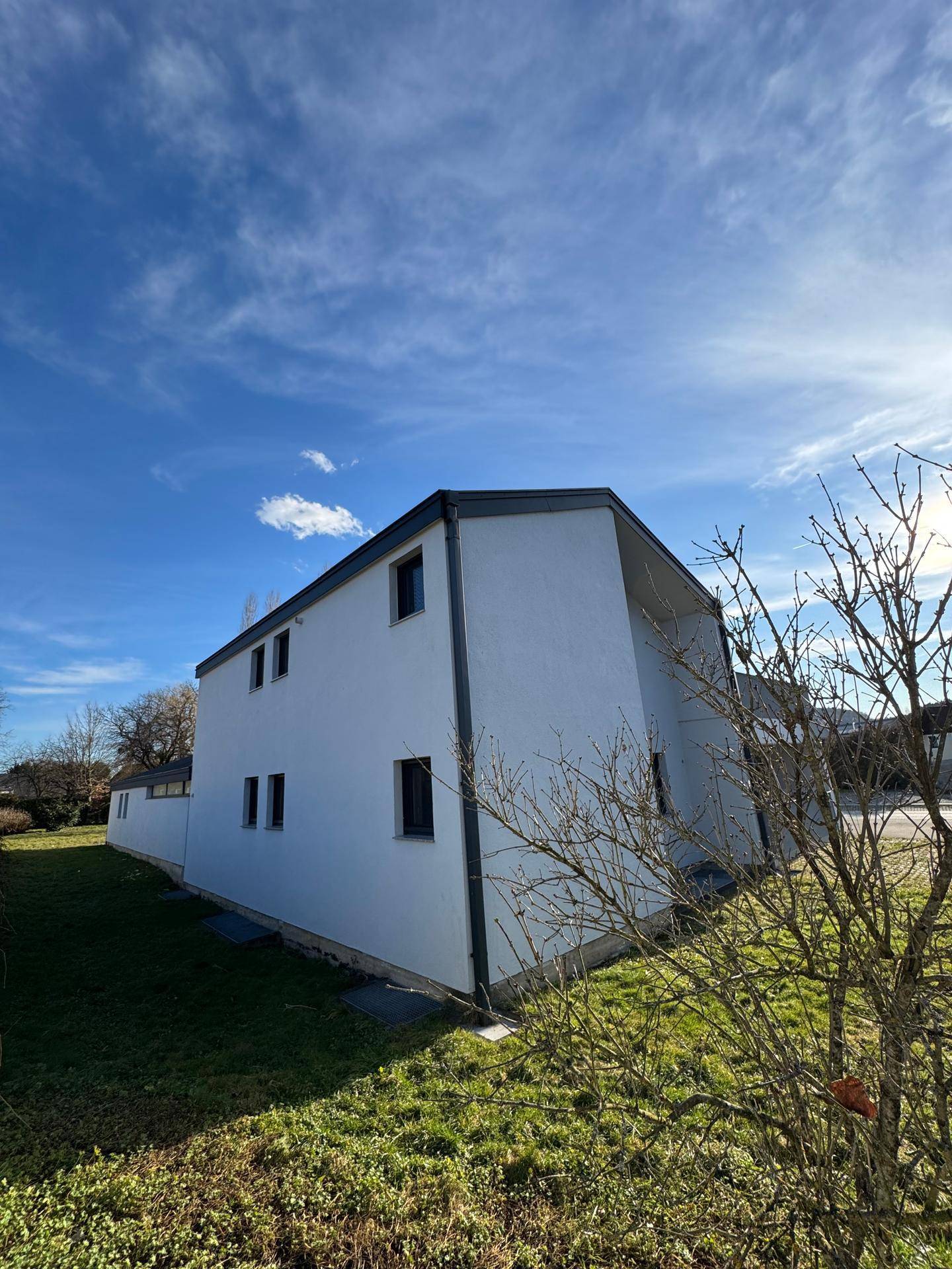 Seitenansicht des modernen Wohnhauses mit weißer Fassade und grünem Rasen.