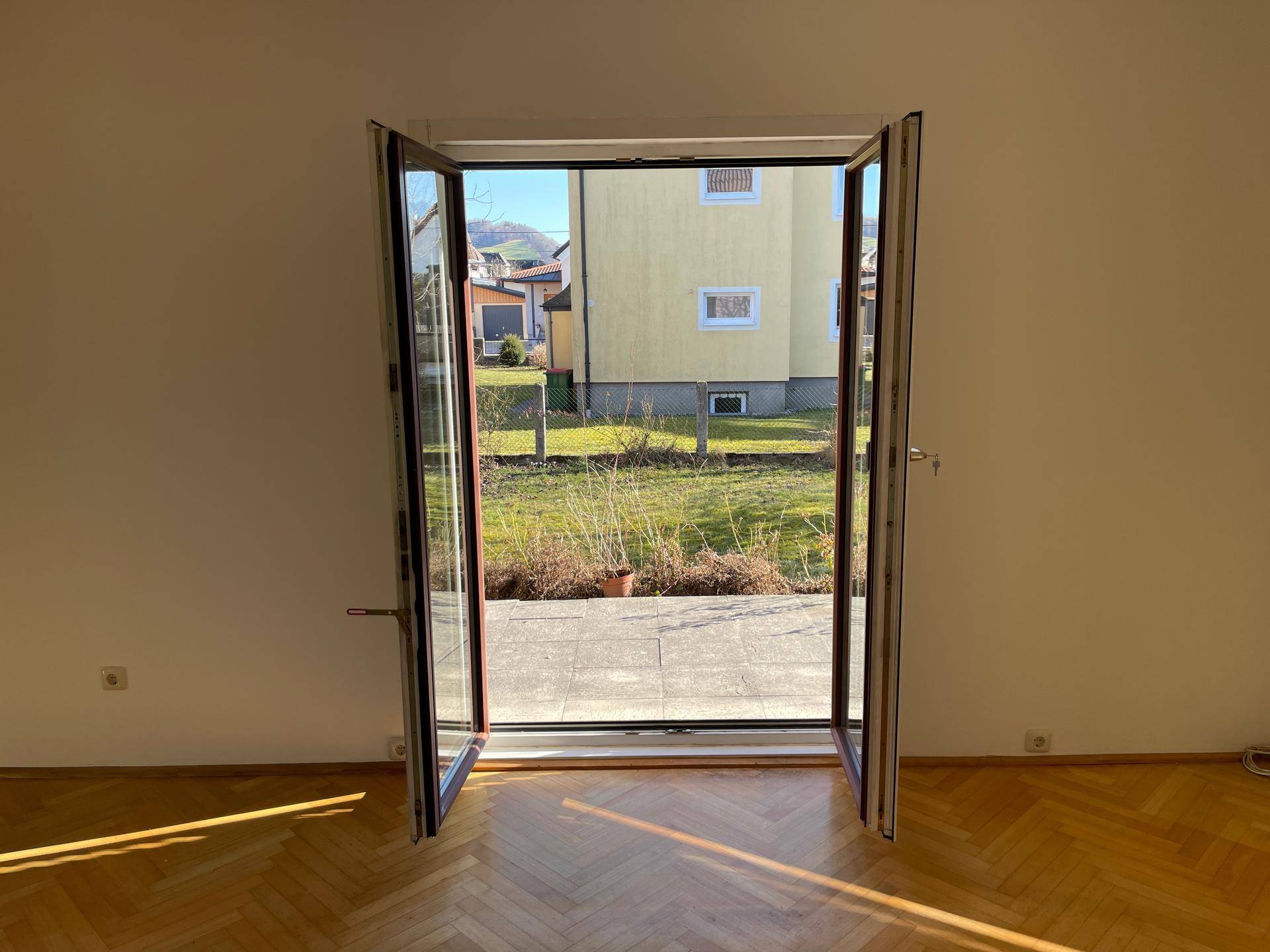 Heller Raum mit Parkettboden und geöffneter Terrassentür zum Garten.