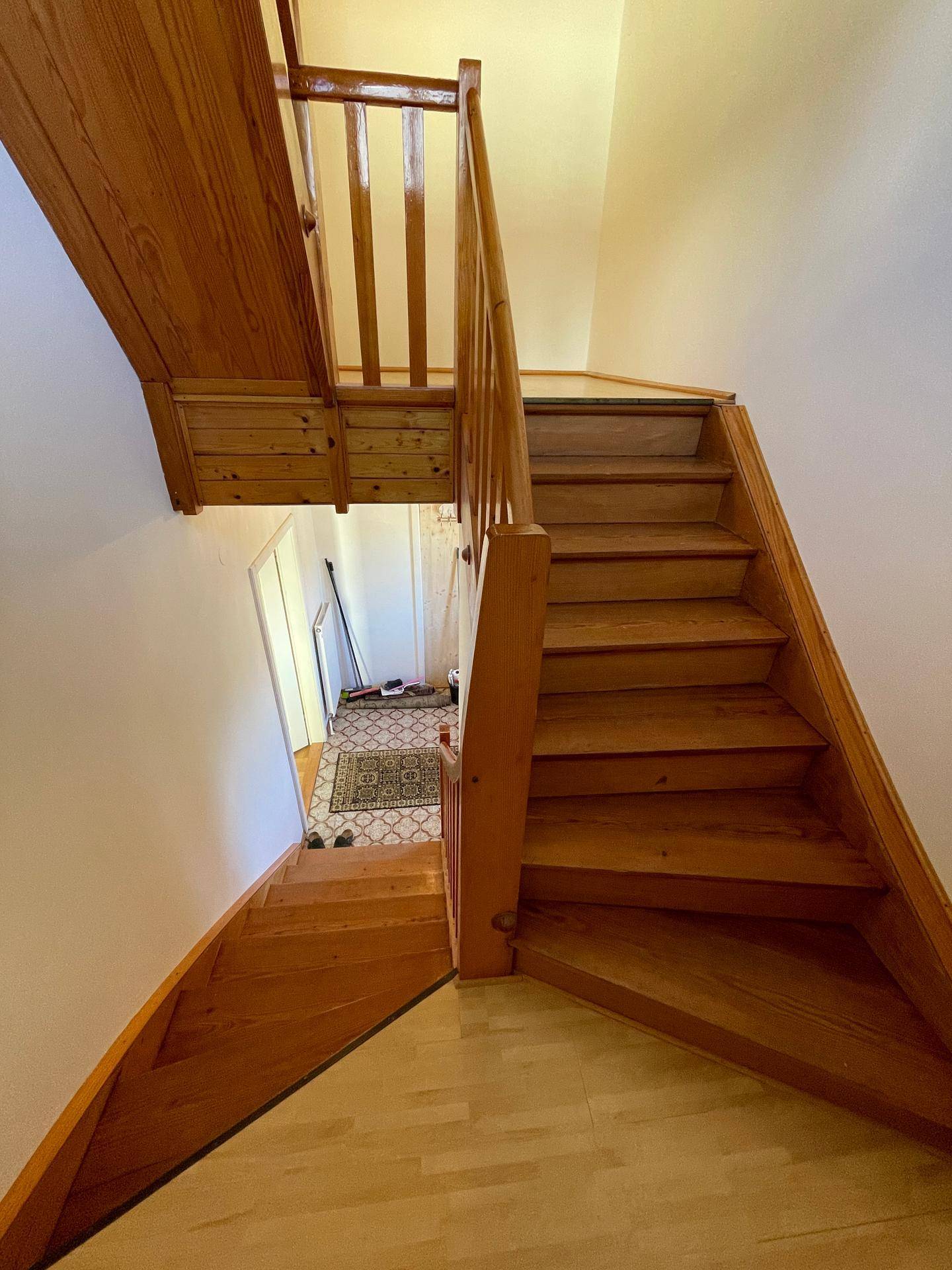 Holztreppe führt in das obere Stockwerk, mit hellem Holzboden im Flur.