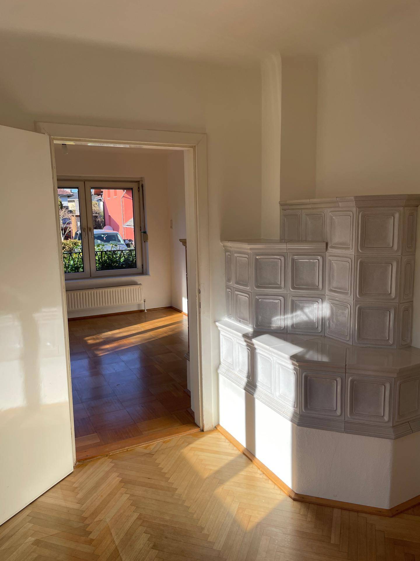 Heller Wohnbereich mit Kachelofen und Blick in ein weiteres Zimmer.