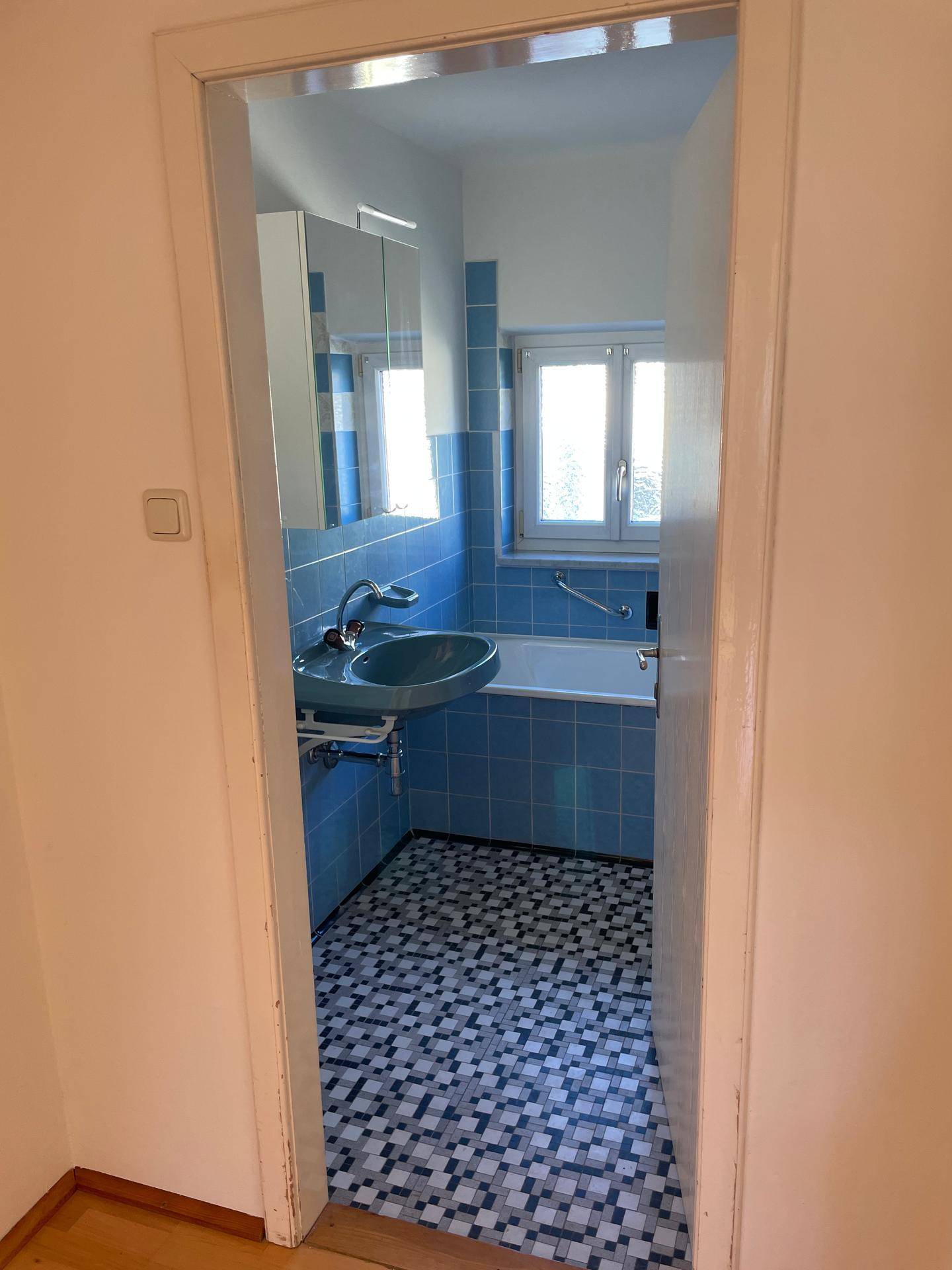 Badezimmer mit blauen Fliesen, Waschbecken, Badewanne und Spiegelschrank.