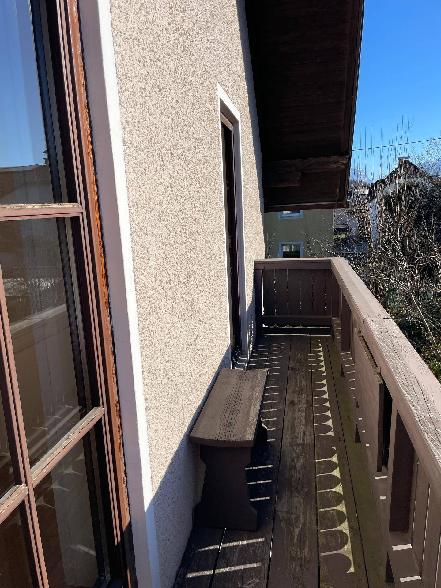 Schmaler Holzbalkon mit Sitzbank und Blick auf die Umgebung.