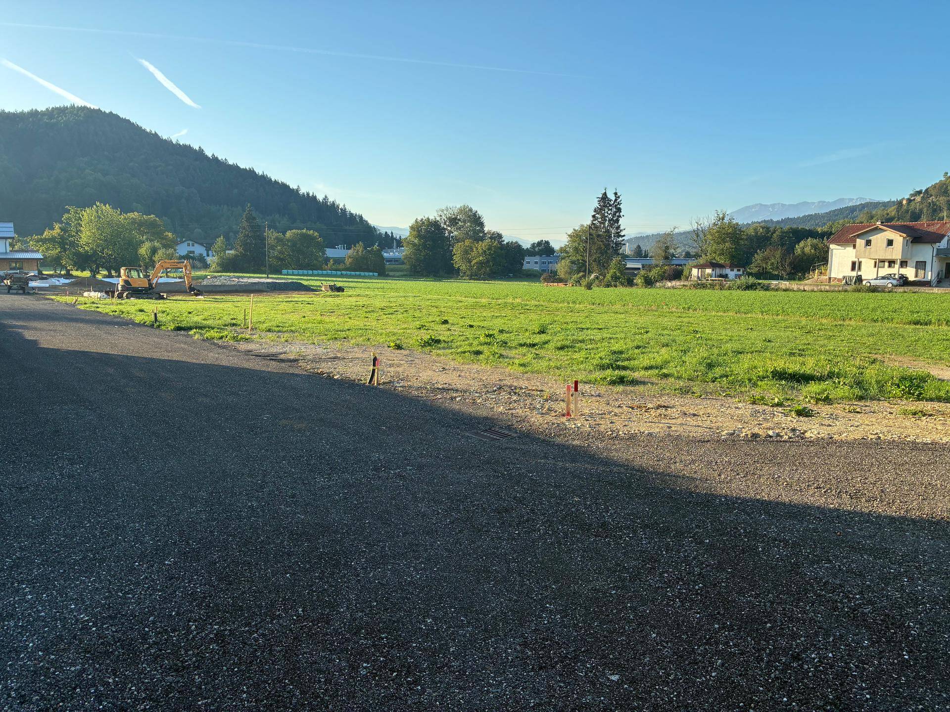 Weitläufiges Grundstück mit Blick auf grüne Hügel und umliegende Häuser in sonniger Lage.