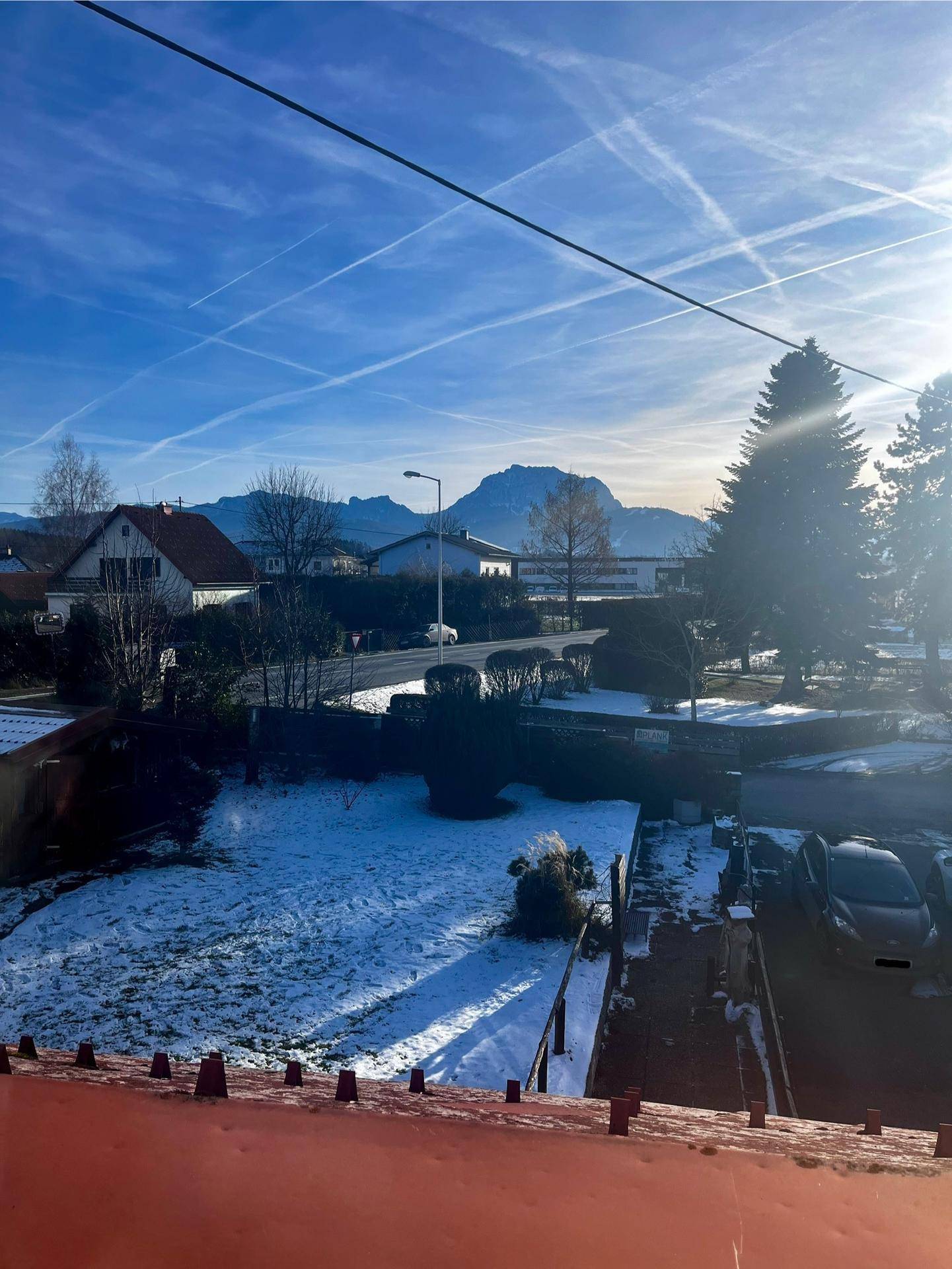 Weitblick über den verschneiten Garten, die Straße und die umliegende Berglandschaft.