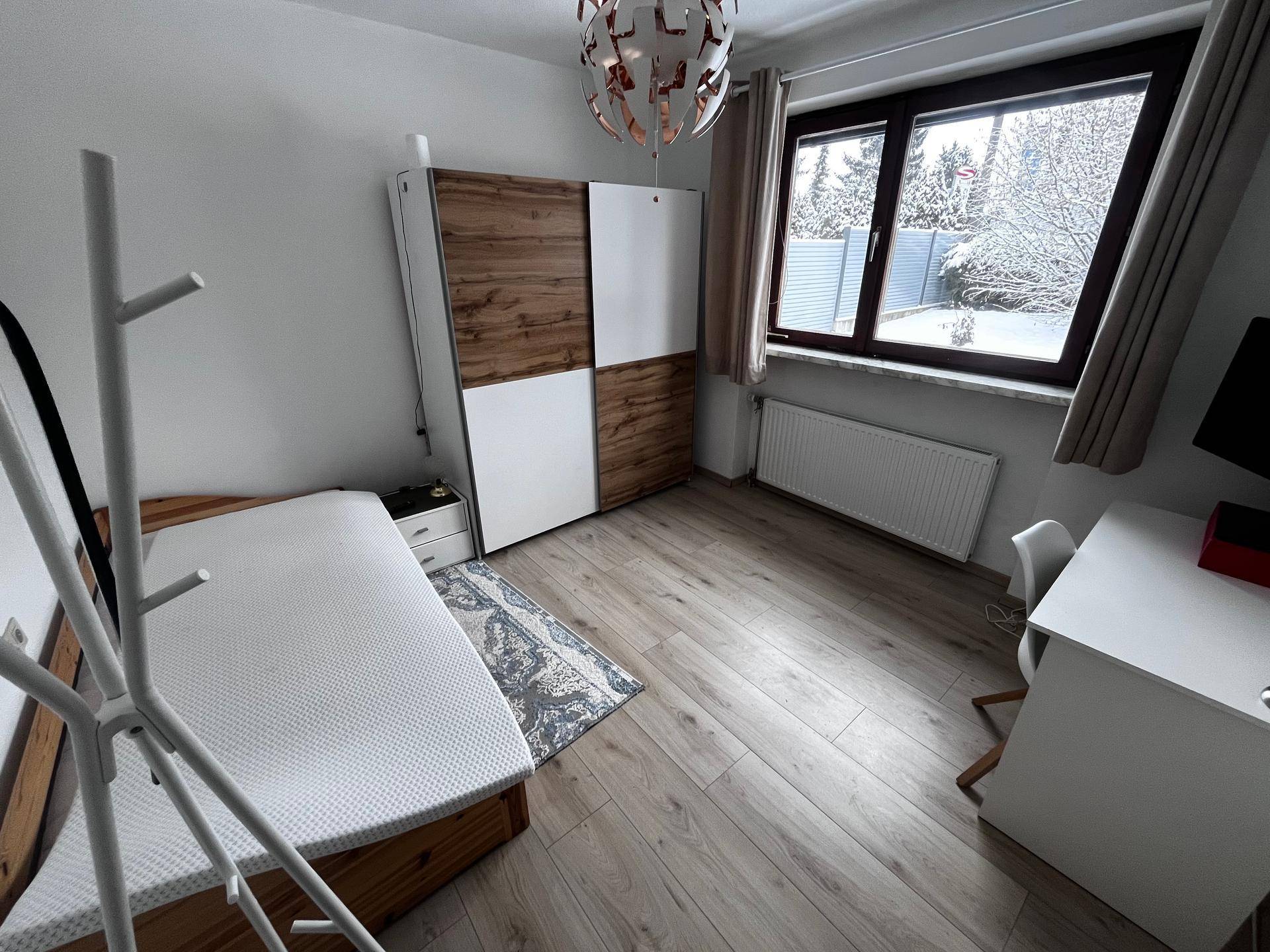 Gemütliches Schlafzimmer mit Bett, Kleiderschrank, Schreibtisch und großem Fenster.