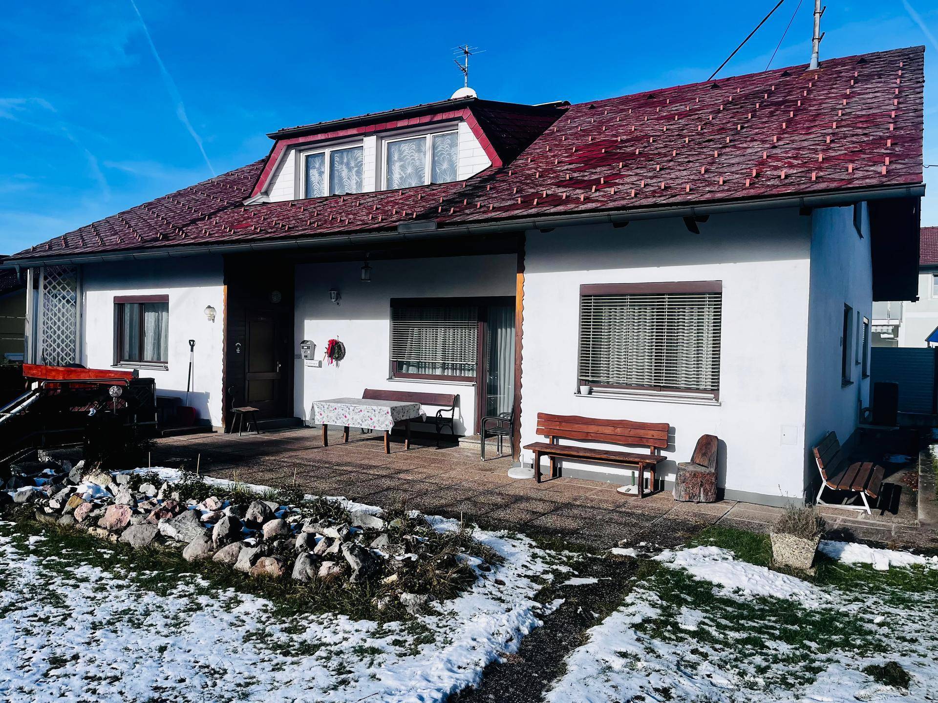 Seitenansicht des Hauses mit gepflastertem Bereich, Sitzbank und verschneitem Garten.