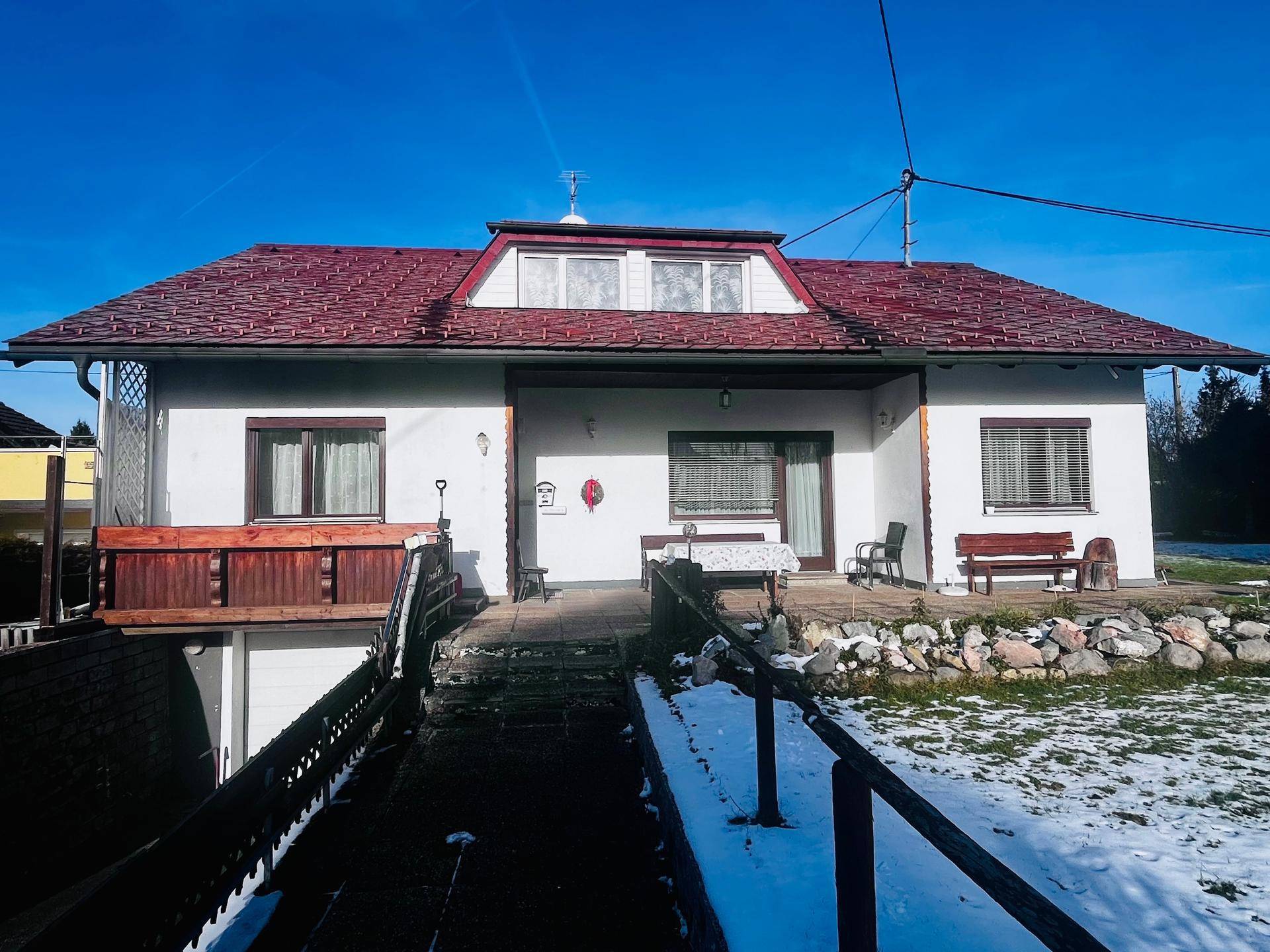 Vorderansicht des Hauses mit rotem Dach, weißer Fassade und verschneitem Gartenbereich.