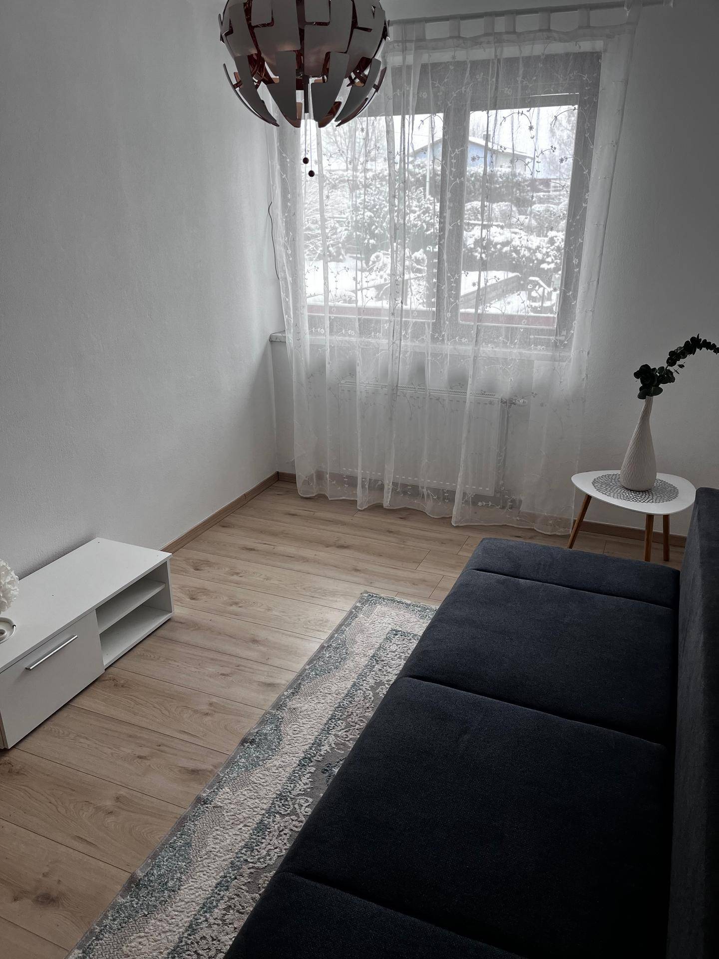 Helles Wohnzimmer mit modernem Sofa, Holzboden und einem Fenster mit Vorhängen.