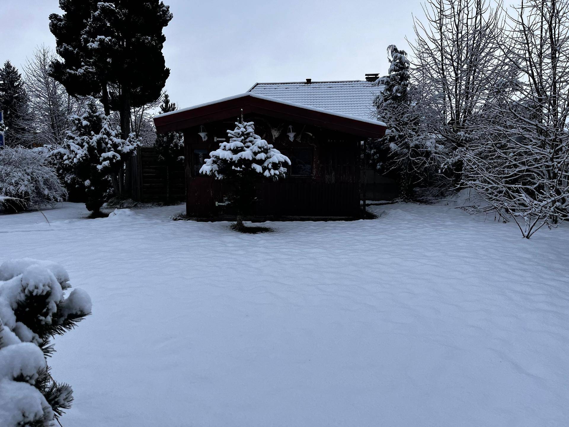 Idyllischer, tief verschneiter Garten mit einem kleinen Holzpavillon im Hintergrund.