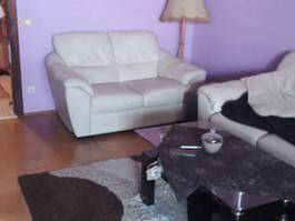 Wohnzimmer mit lila Wänden, weißem Ledersofa und Couchtisch.