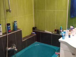 Badezimmer mit grünen und braunen Fliesen, Badewanne und Duscharmatur.