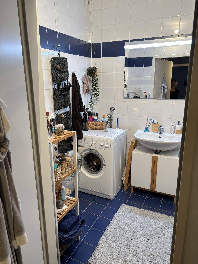 Badezimmer mit Waschmaschine, Waschbecken und blauen Bodenfliesen, funktional eingerichtet.