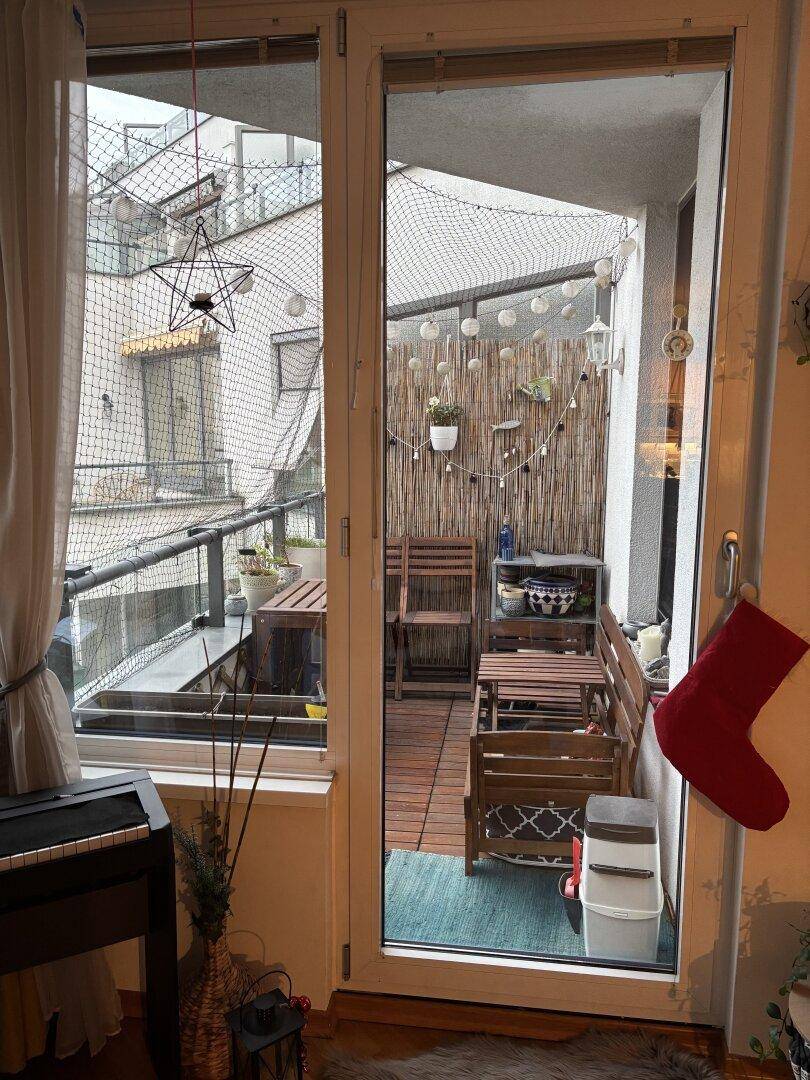 Gemütlicher Balkon mit Holzmöbeln und Dekoration, geschützt durch ein Netz, bietet einen Blick auf die Umgebung.