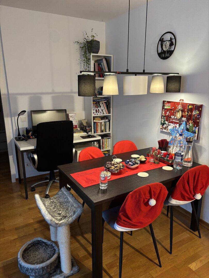 Essbereich mit dunklem Tisch und Stühlen, daneben ein Arbeitsplatz mit Regal und Bürostuhl.