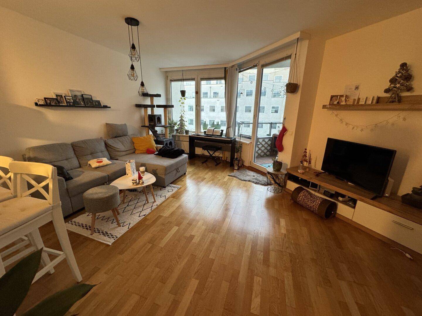 Gemütliches Wohnzimmer mit Sofa, Fernseher und Zugang zum Balkon, dekoriert für die Weihnachtszeit.