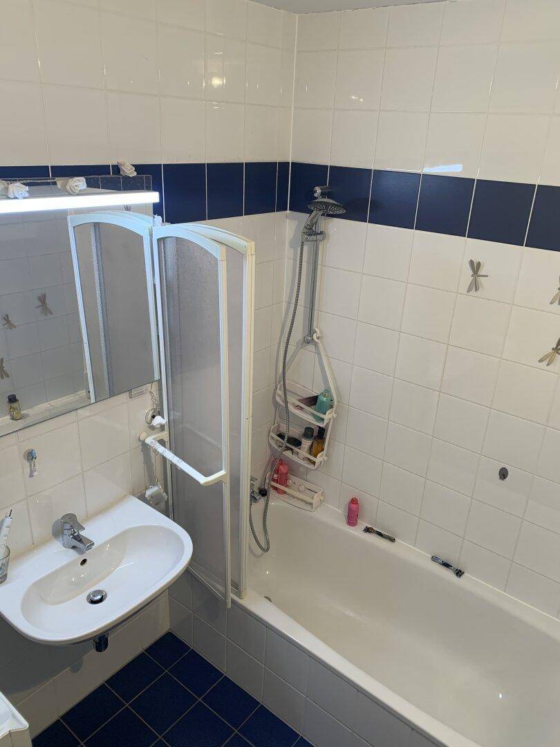 Badezimmer mit Badewanne, Duschvorrichtung und Waschbecken, gefliest in Weiß und Blau.