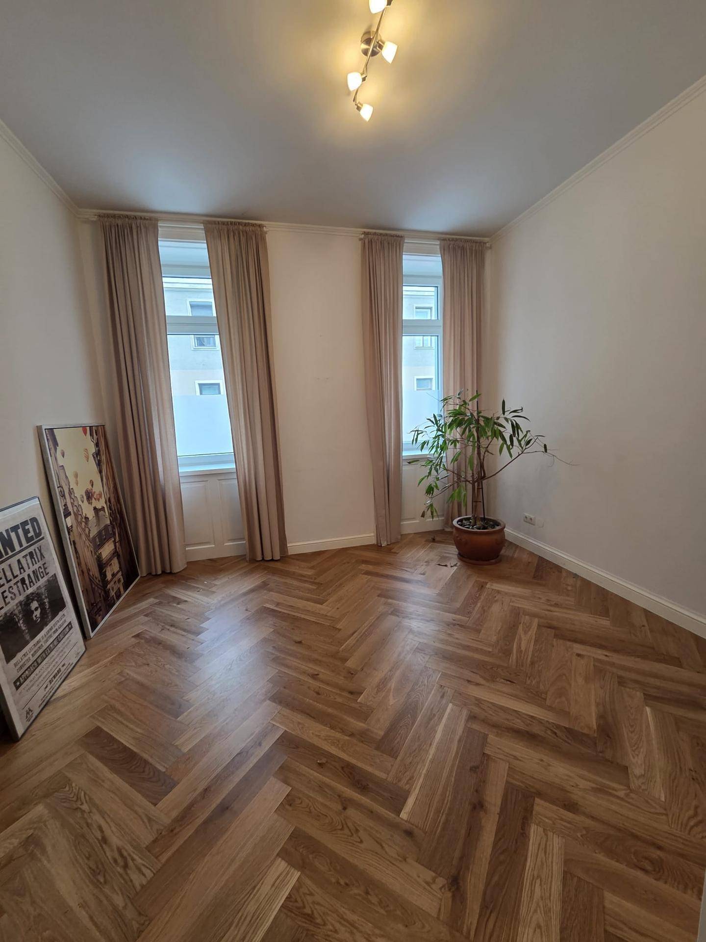Geräumiges Zimmer mit elegantem Fischgrätparkett, zwei großen Fenstern und viel Tageslicht.
